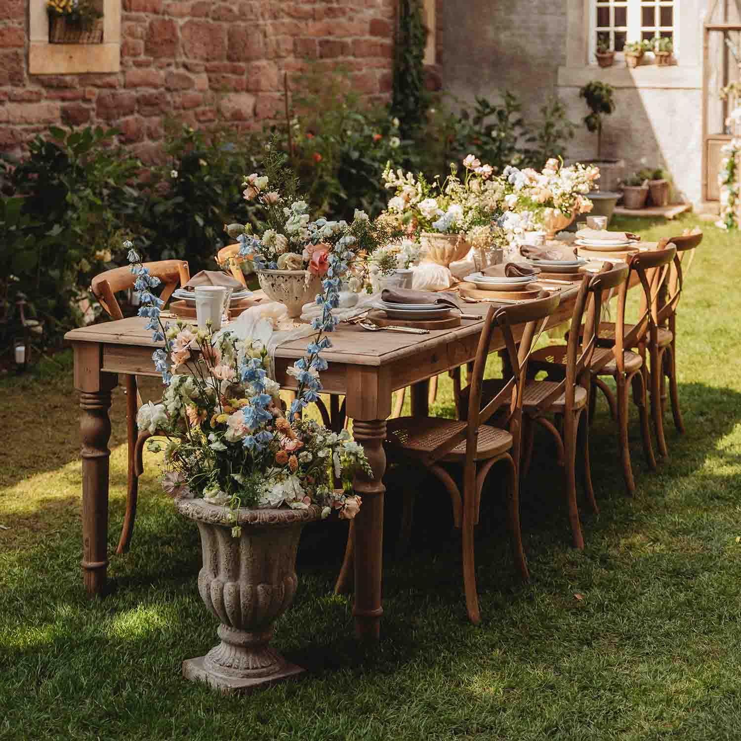 Dřevěný zahradní stůl s květinovou výzdobou a prostřením na trávníku za slunečného dne