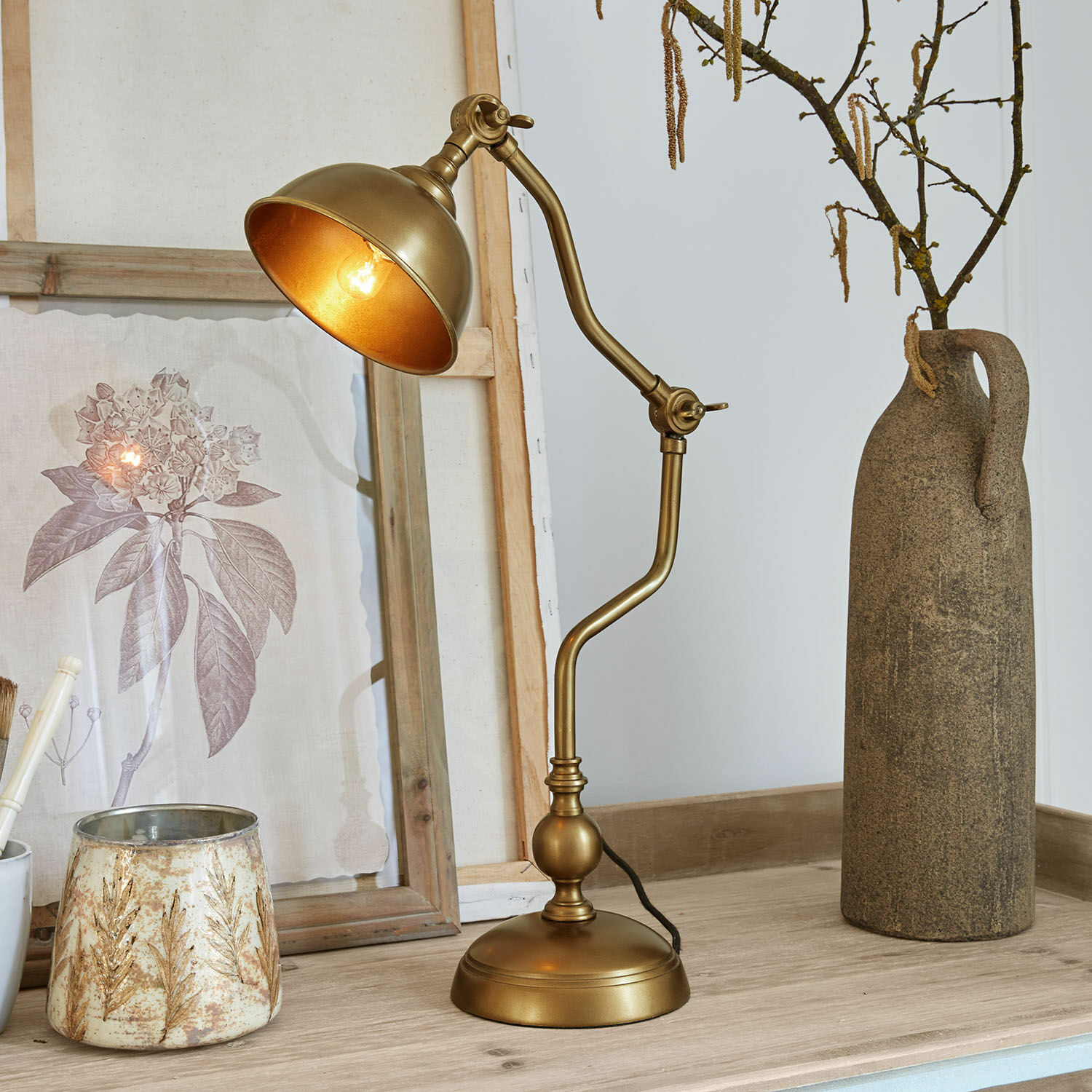 Zlatá kovová stolní lampa s nastavitelným ramenem na dřevěném stole s dekoracemi