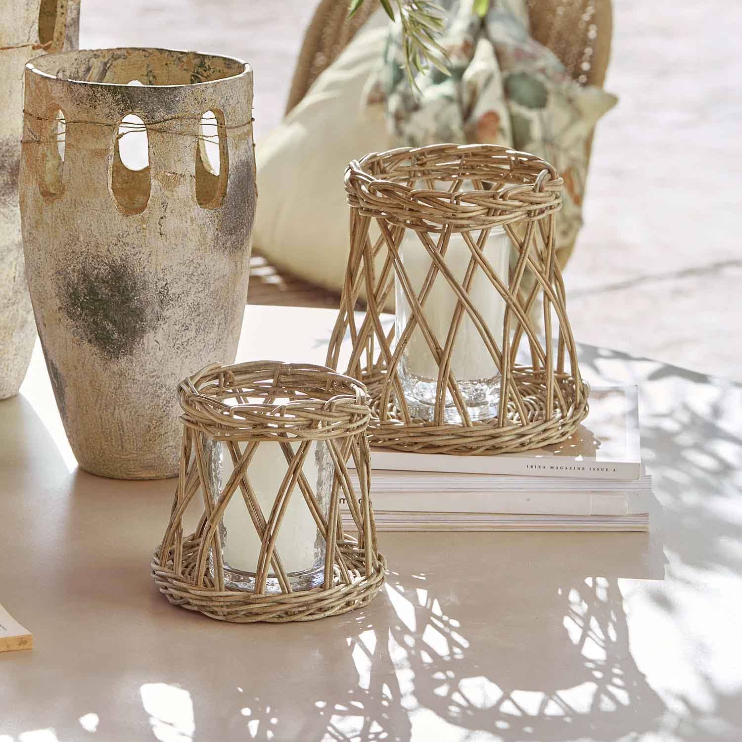 Dvě lucerny z přírodního ratanu s bílými svíčkami na světlém stole, interiérová dekorace