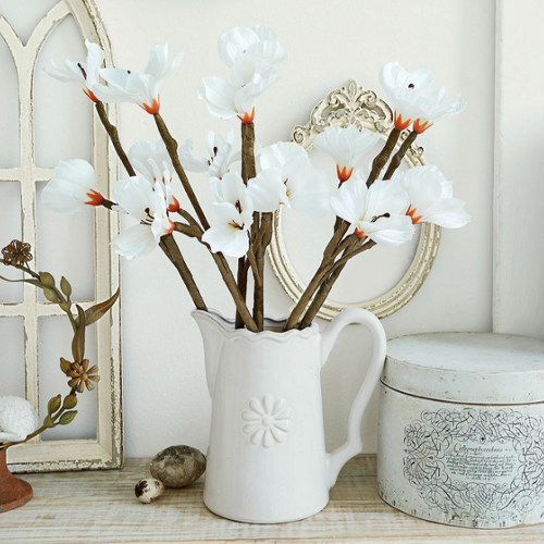 Bílá keramická konvice s dekorativními květy na dřevěném stole, vintage styl, interiérová dekorace