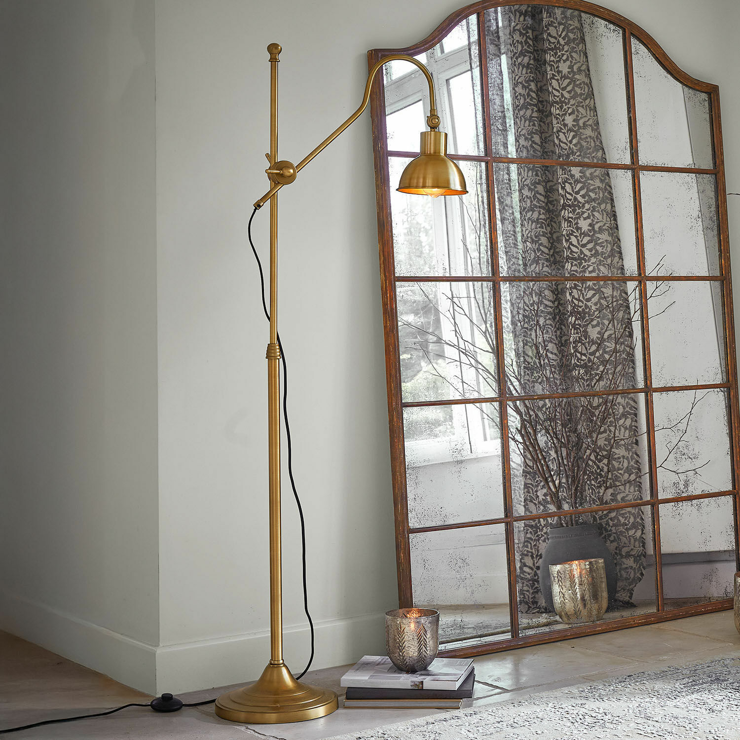 Stojací lampa Delacroille Zlatá kovová stojací lampa s nastavitelným ramenem vedle velkého vintage zrcadla