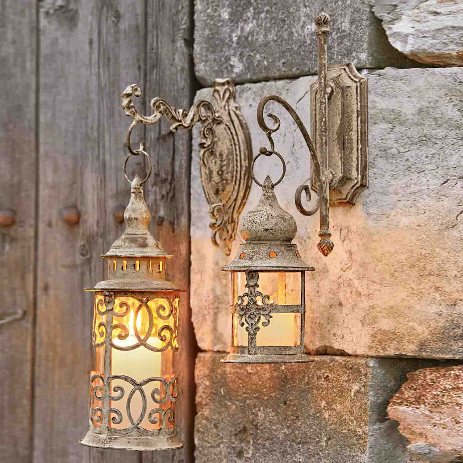 Dvě rustikální nástěnné lampy z kovu v patinované béžové barvě osvětlující kamennou zeď