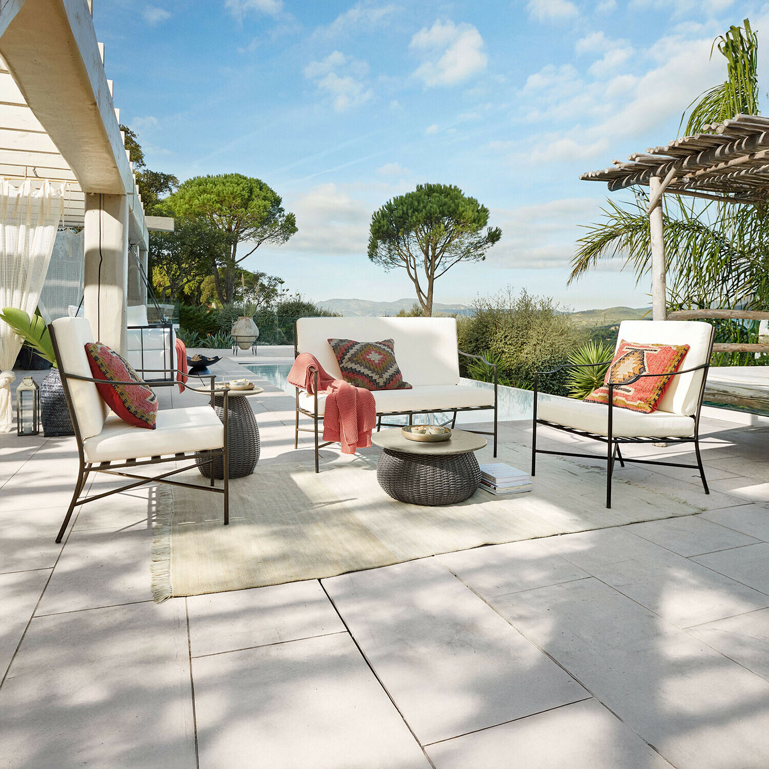 Sada zahradního nábytku s kovovými rámy a krémovými polštáři na terase s výhledem na bazén