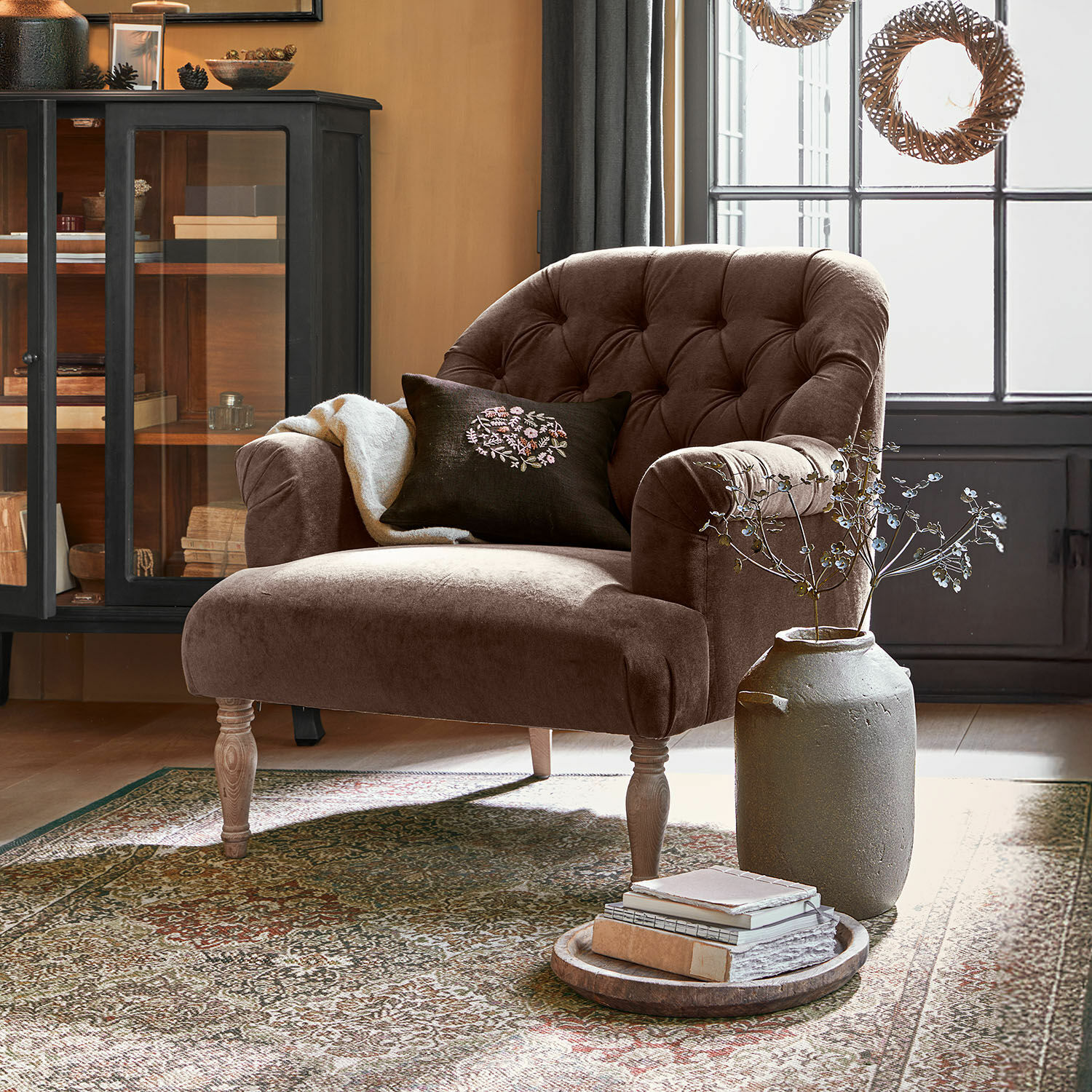 Křeslo Shambrook Hnědé sametové křeslo s prošívaným opěradlem a dřevěnými nohami v útulném obývacím pokoji s kobercem