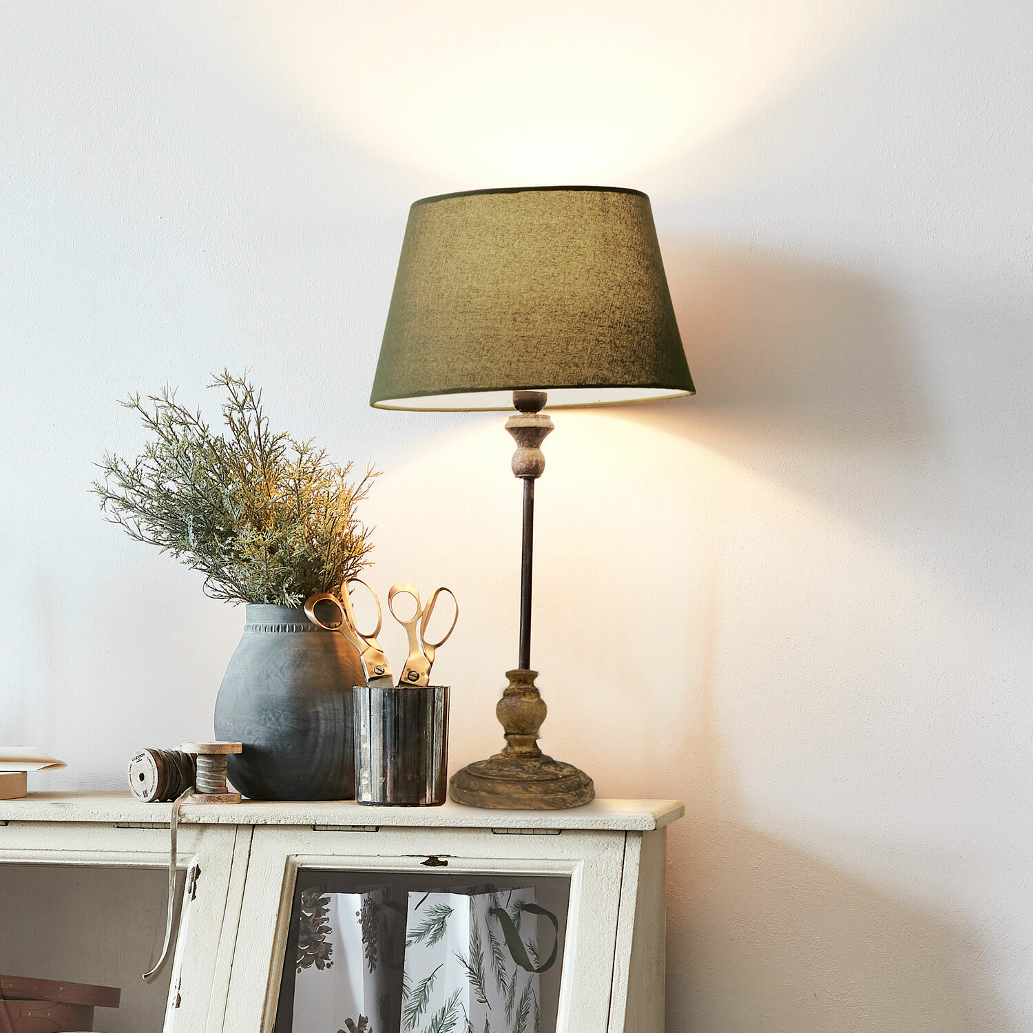 Stolní lampa Karlora Stolní lampa se zeleným stínidlem a dřevěným podstavcem na bílé komodě s dekorací