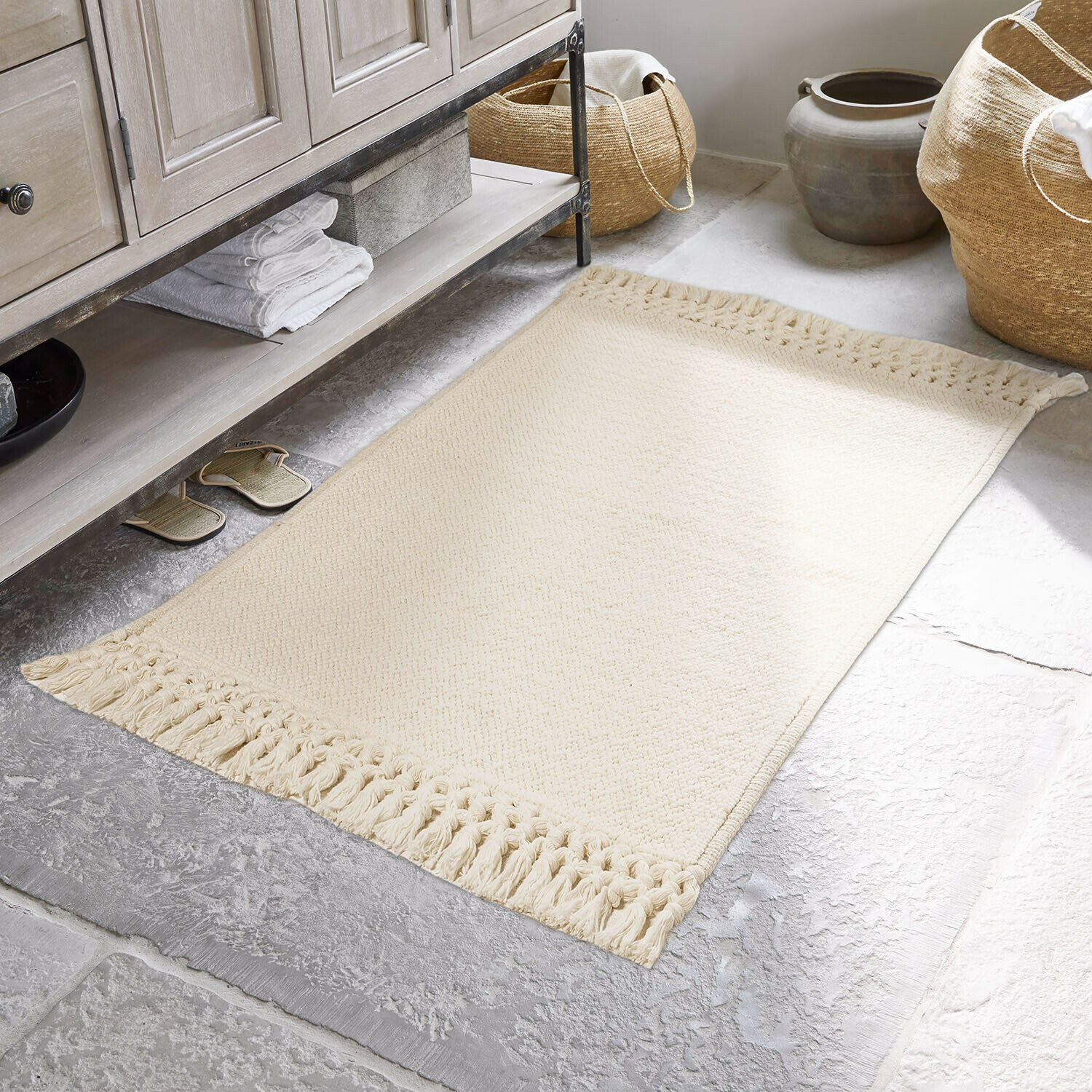 Béžový bavlněný koberec s třásněmi na kamenné podlaze v koupelně, interiérová dekorace