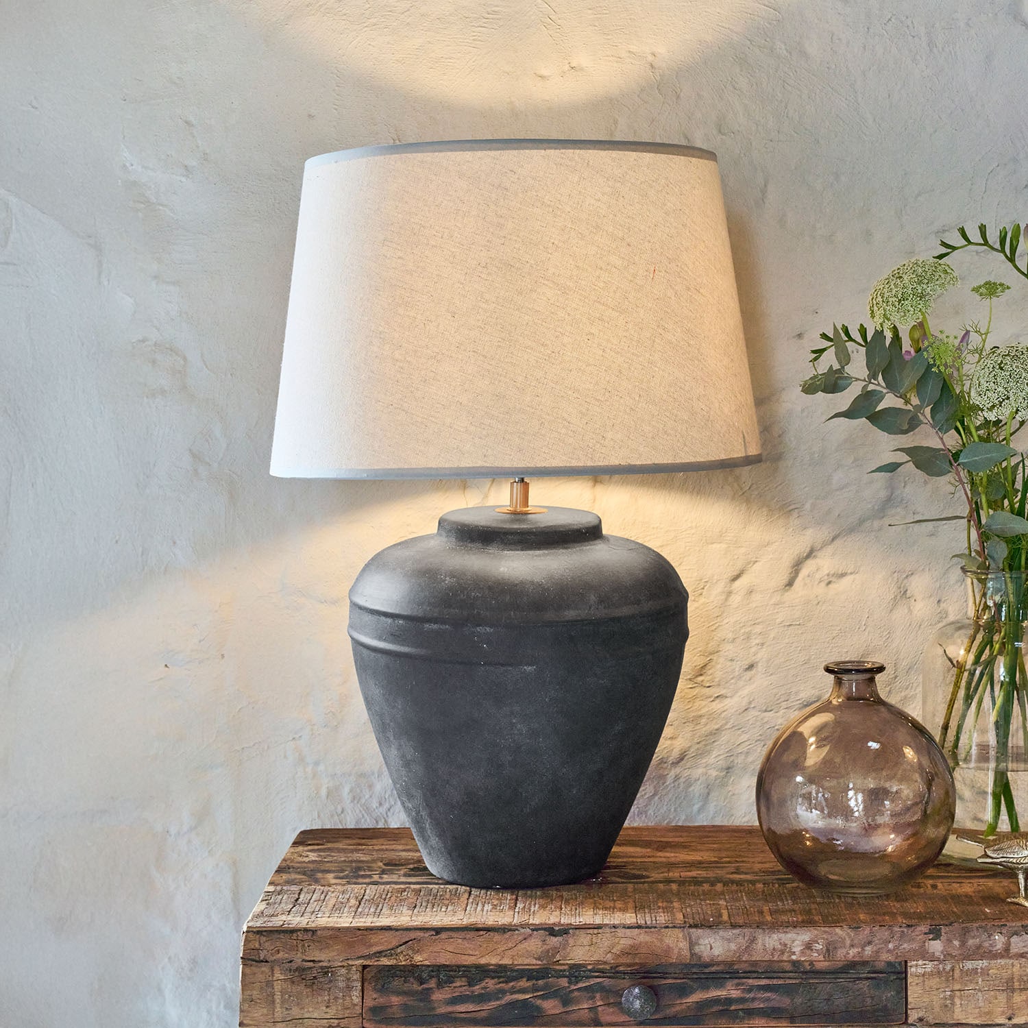 Stolní lampa z černé keramiky s béžovým stínidlem na dřevěném stole, interiérová dekorace