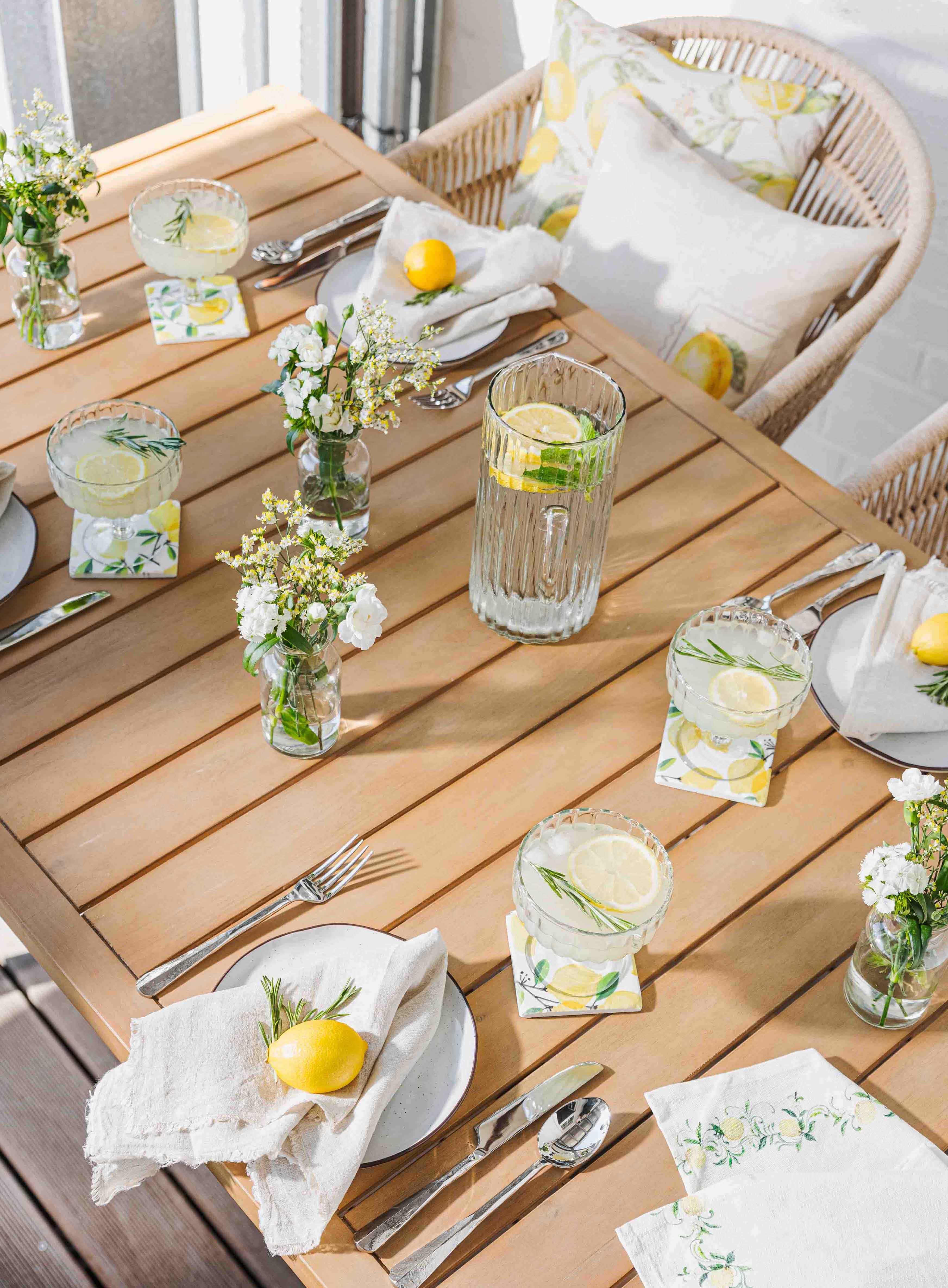 Světle dřevěný stůl s limonádou, sklenicemi a citronovou dekorací pro letní zahradní posezení