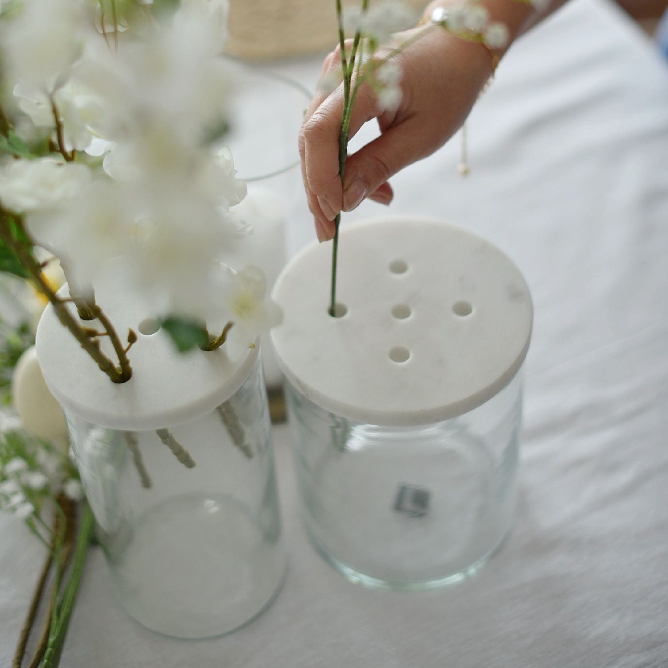 Skleněná váza s bílým mramorovým víkem s otvory pro aranžování květin na stole