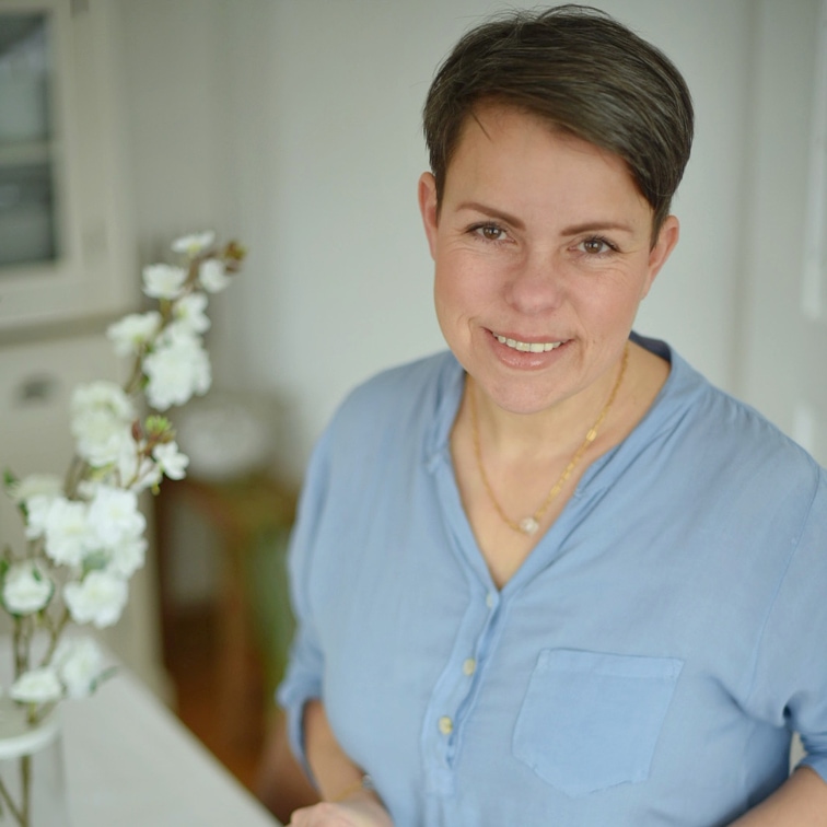 Usměvavá žena v modré košili vedle bílých květin v světlém interiéru