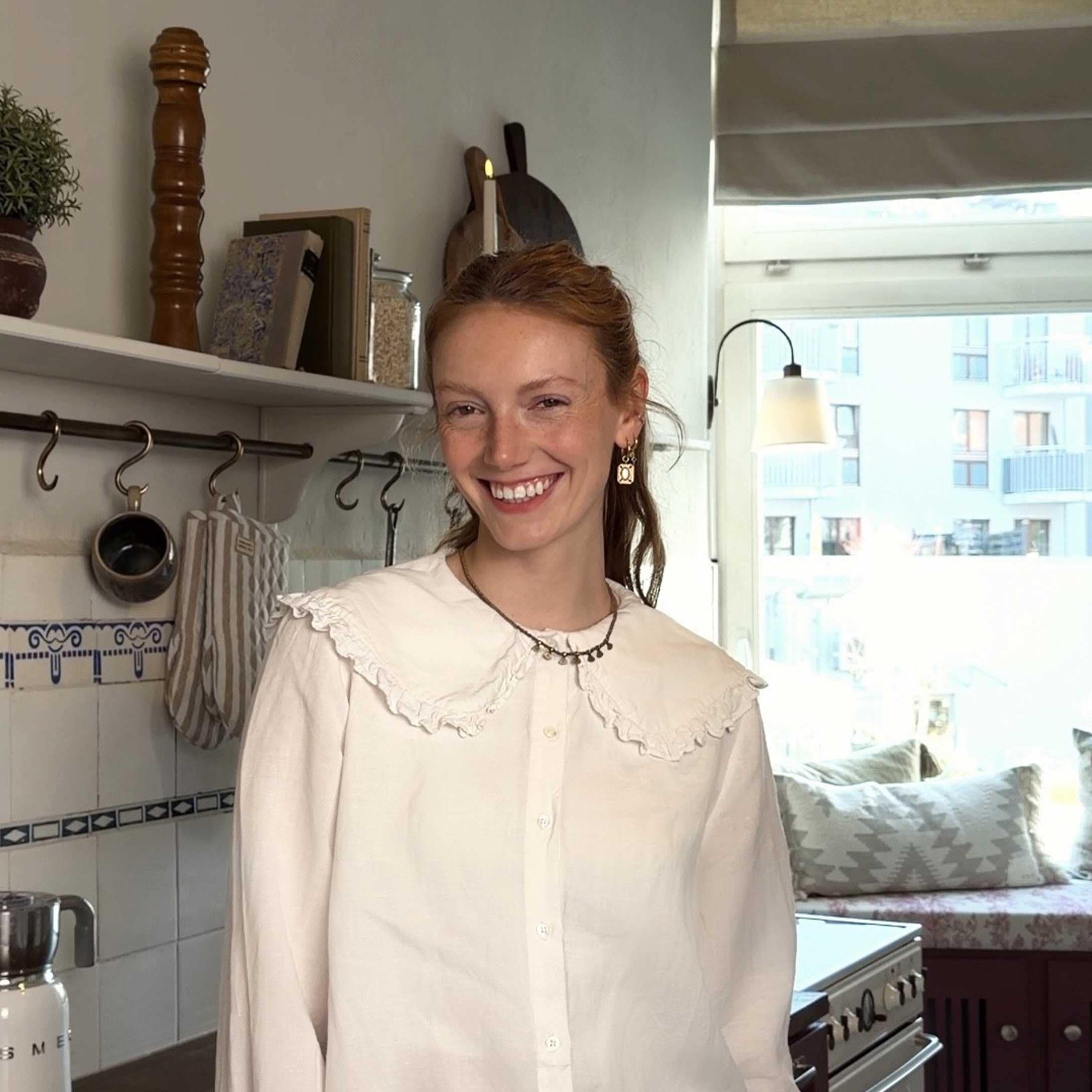 Žena v bílé blůze s volánky v světlé kuchyni s dekorativními doplňky a oknem