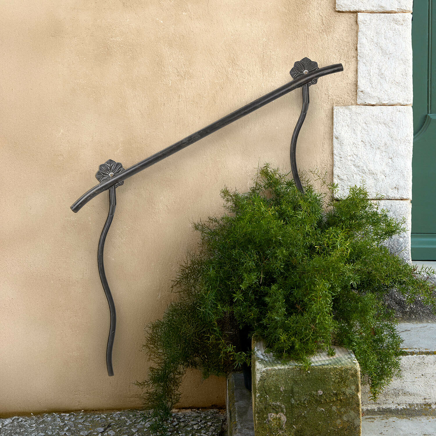 Černé kovové zábradlí s ozdobnými držáky na béžové zdi u schodů s zelenými rostlinami