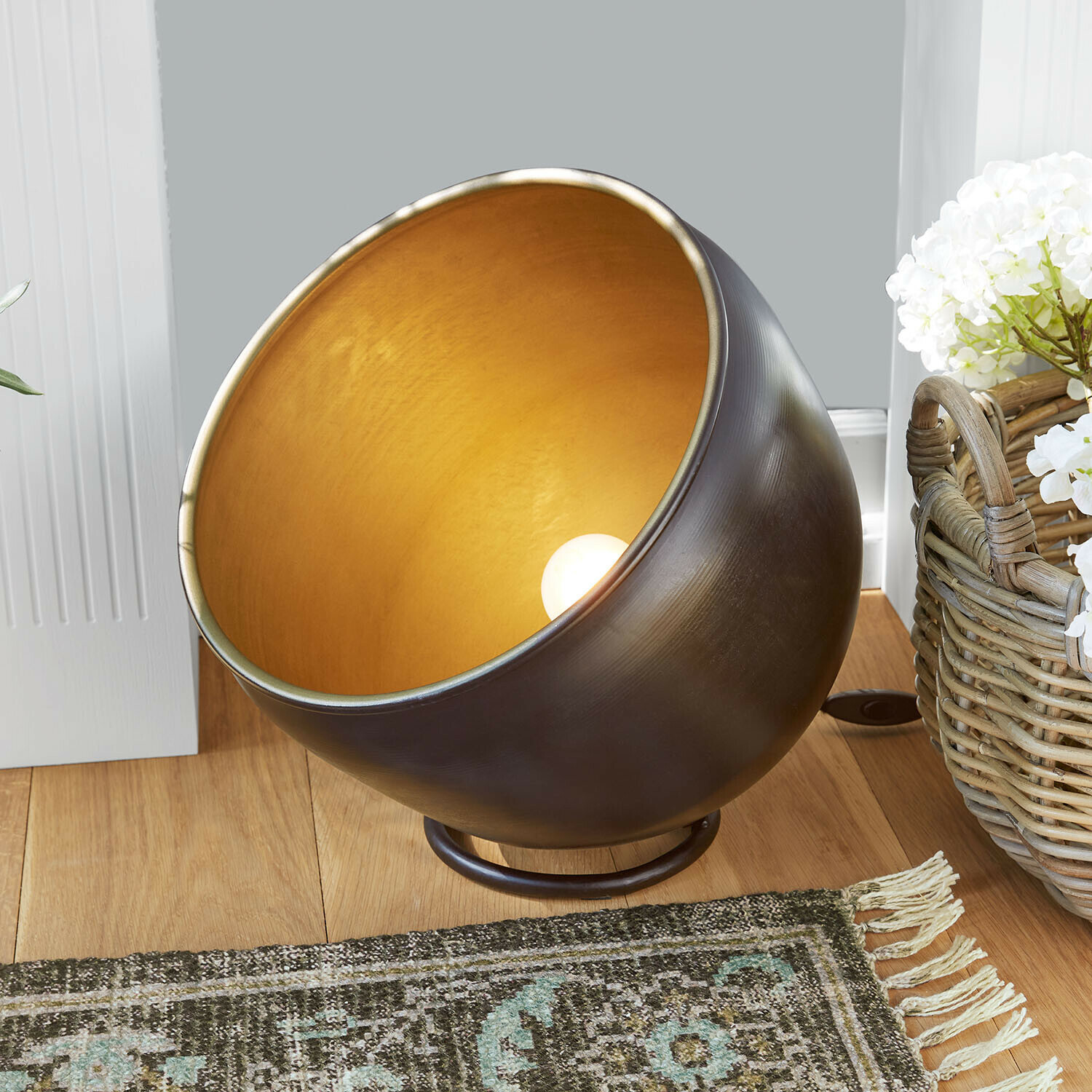 Kovová stolní lampa se zlatým vnitřkem a černým povrchem na dřevěné podlaze