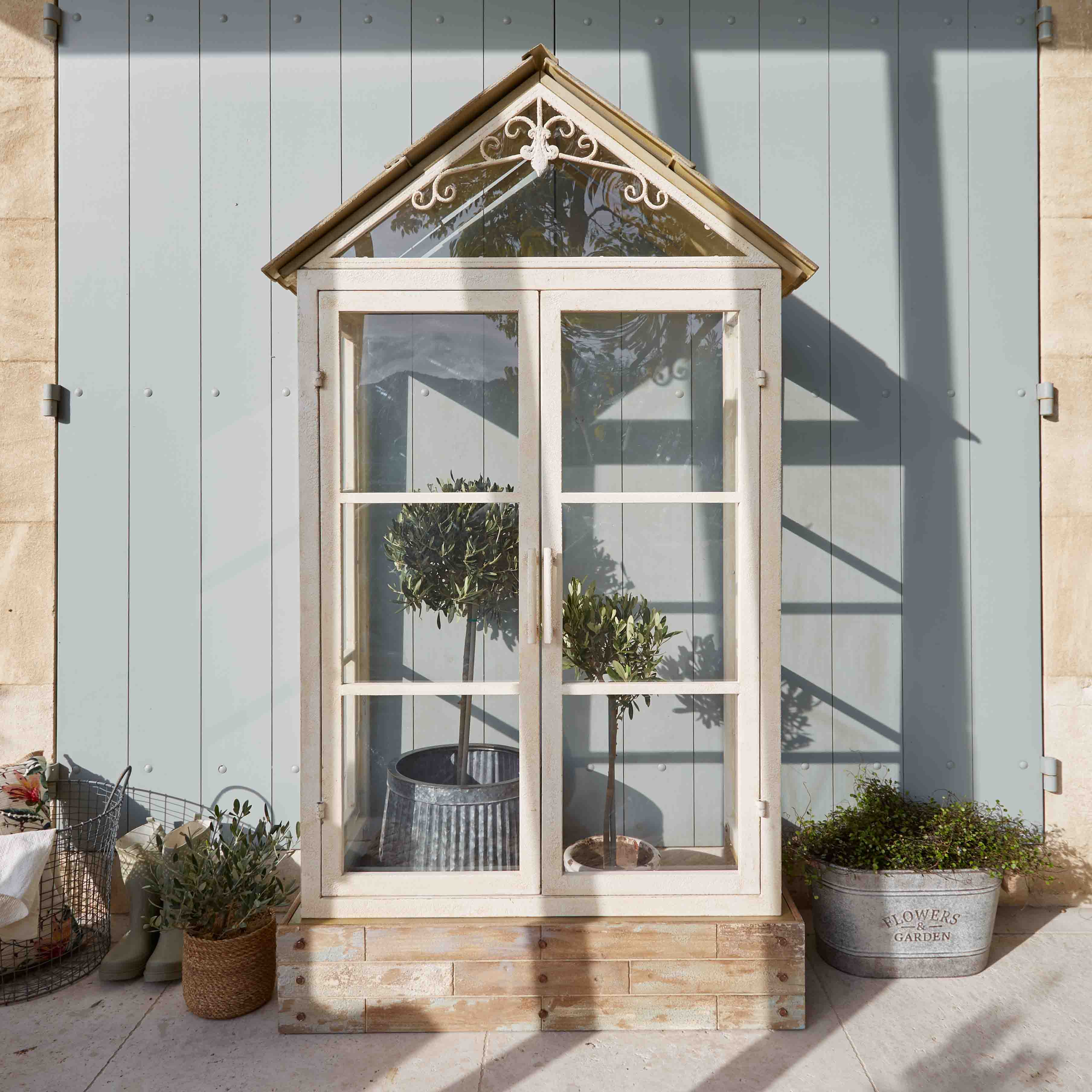 Bílá dřevěná skleník s dekorativní střechou a rostlinami v květináčích na terase