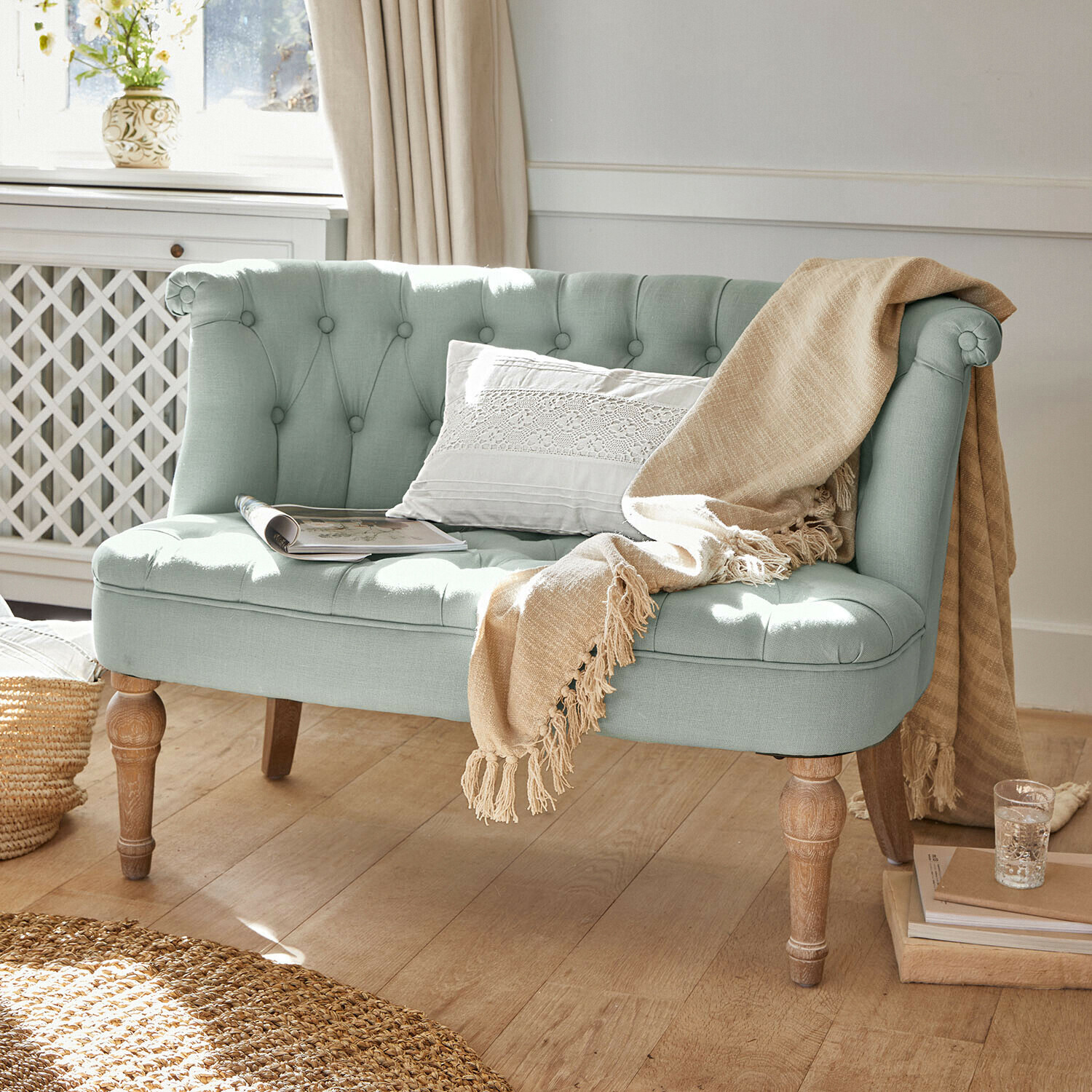 Mátově zelená čalouněná pohovka s dřevěnými nohami, béžovou dekou a bílým polštářem ve vintage stylu