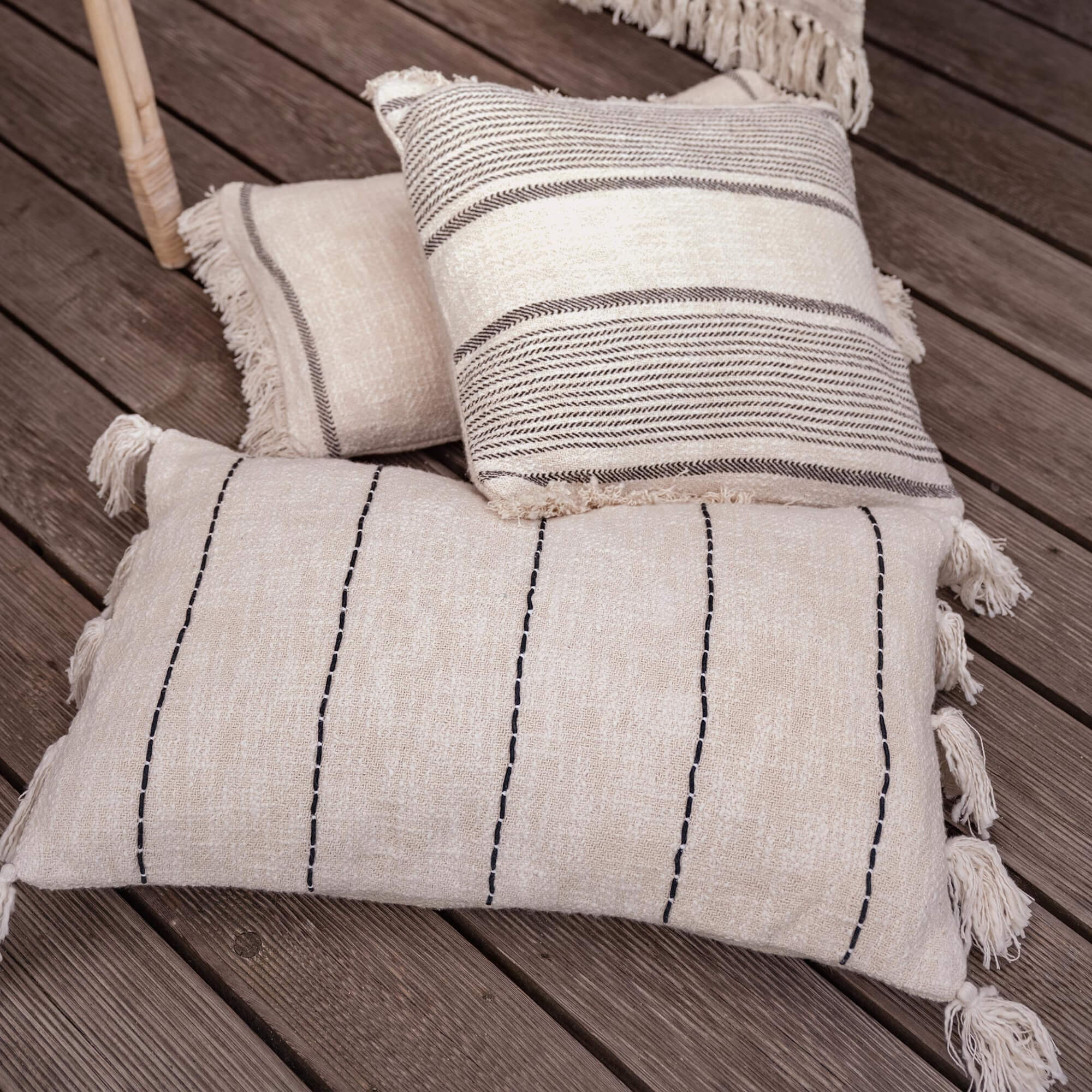 Sada tří krémových dekorativních polštářů s třásněmi a vzory na dřevěné podlaze