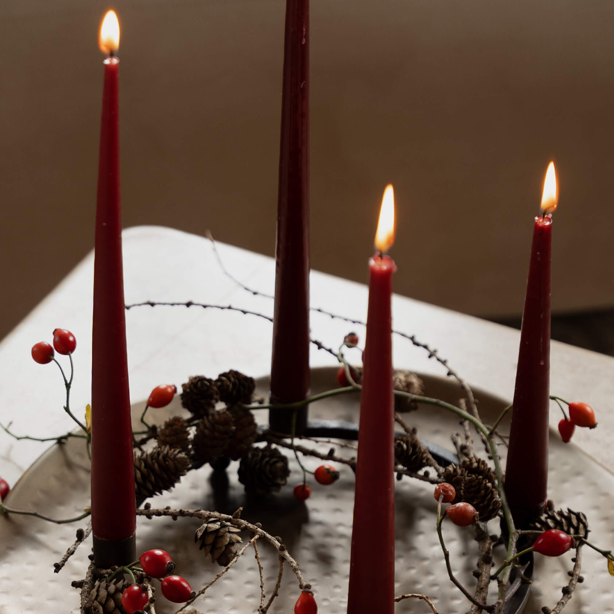 Červené adventní svíčky na kovovém věnci s šiškami a červenými plody na stole