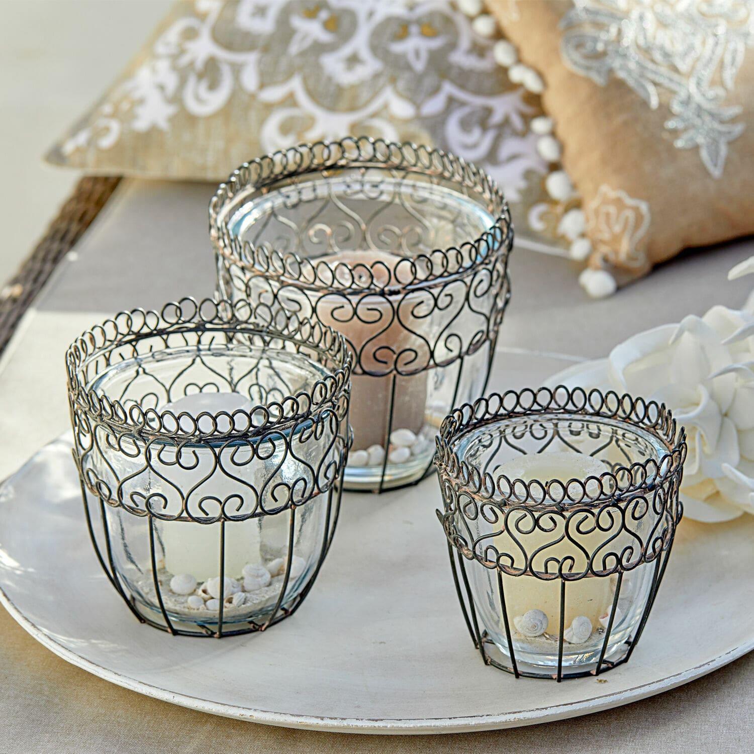 Sada tří skleněných svícnů s černým kovovým rámem a dekorativními vzory na tácu