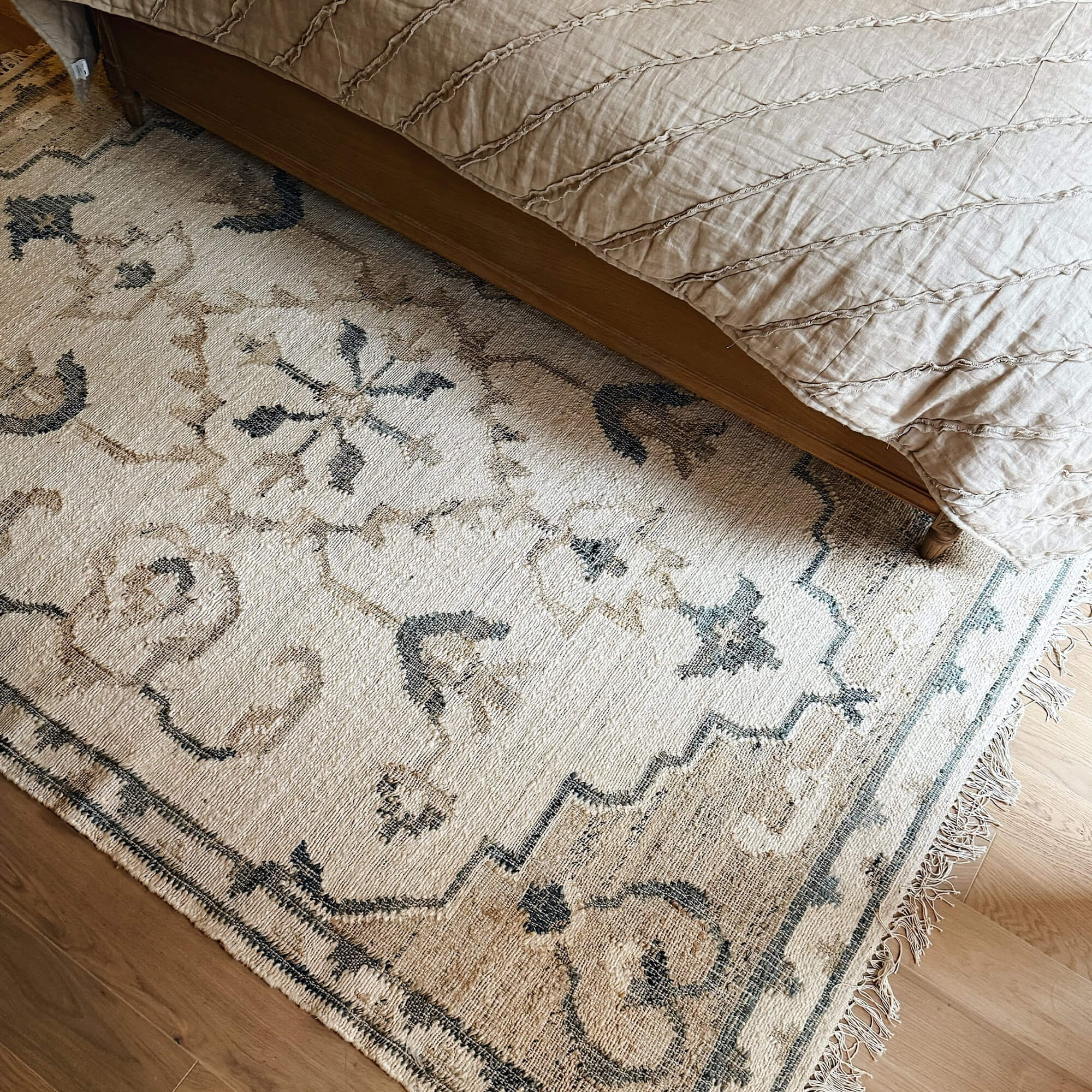 Béžový koberec s orientálním vzorem a třásněmi na dřevěné podlaze u postele