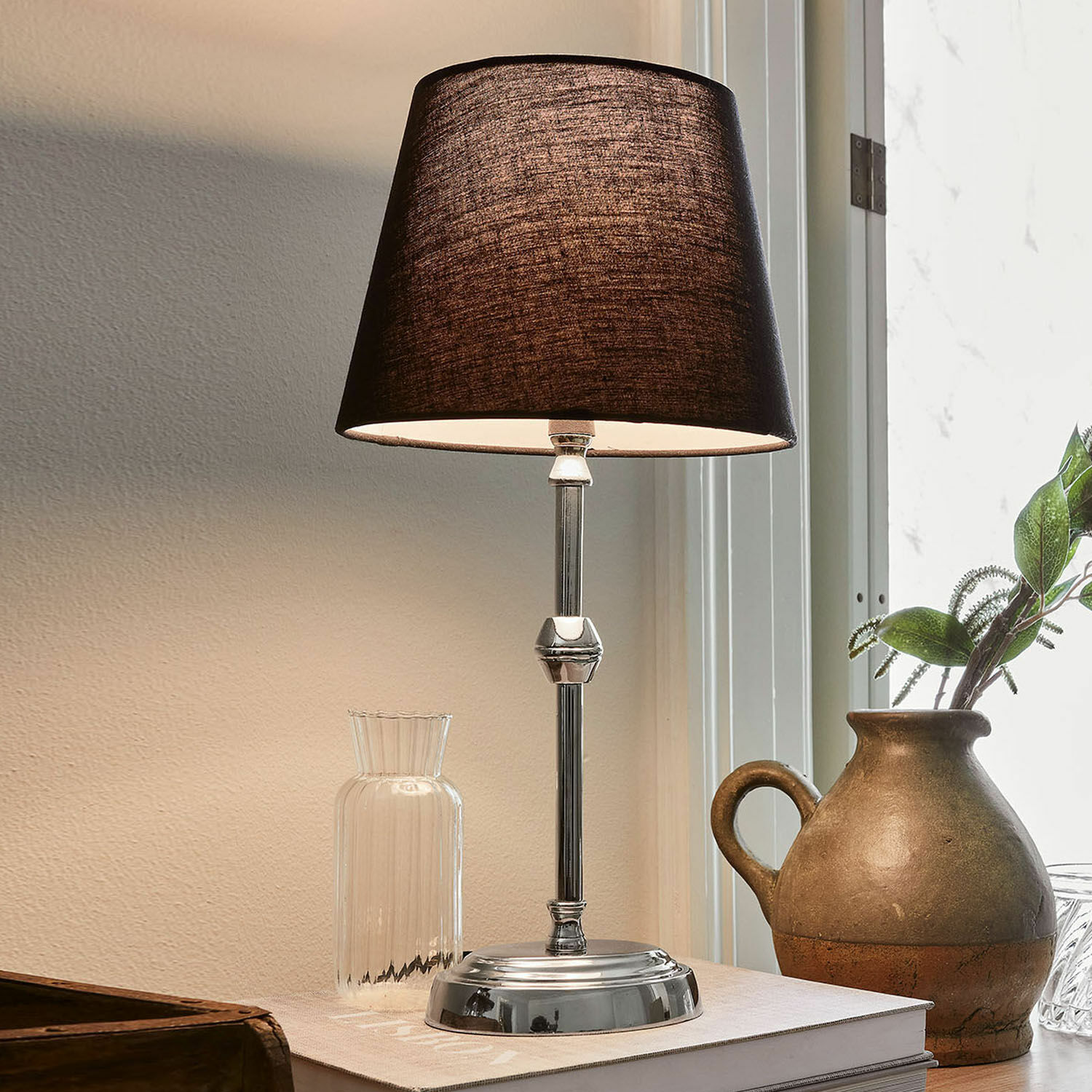 Stolní lampa Luceau Elegantní stolní lampa s kovovým podstavcem a černým stínidlem na stole s dekorací