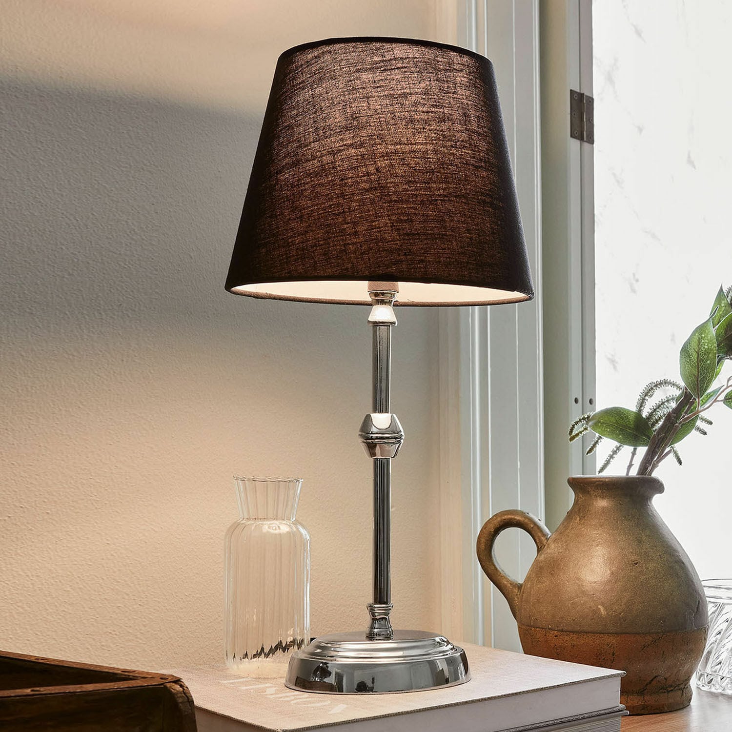 Stolní lampa Luceau Elegantní stolní lampa s kovovým podstavcem a černým stínidlem na stole s dekorací