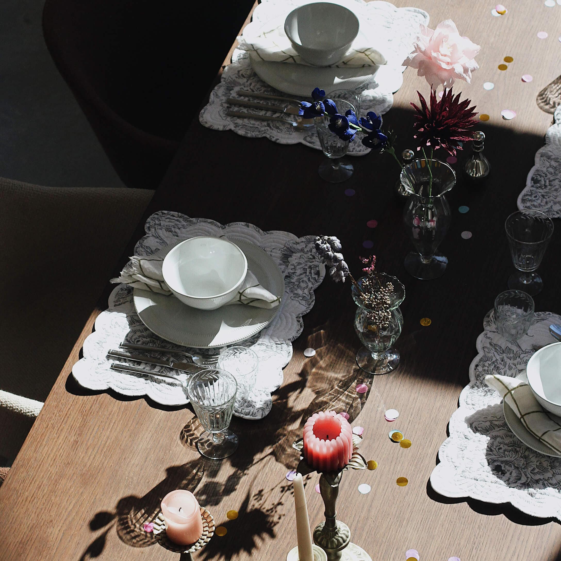 Elegantně prostřený stůl s bílým porcelánem, sklenicemi a svíčkami na dřevěném povrchu