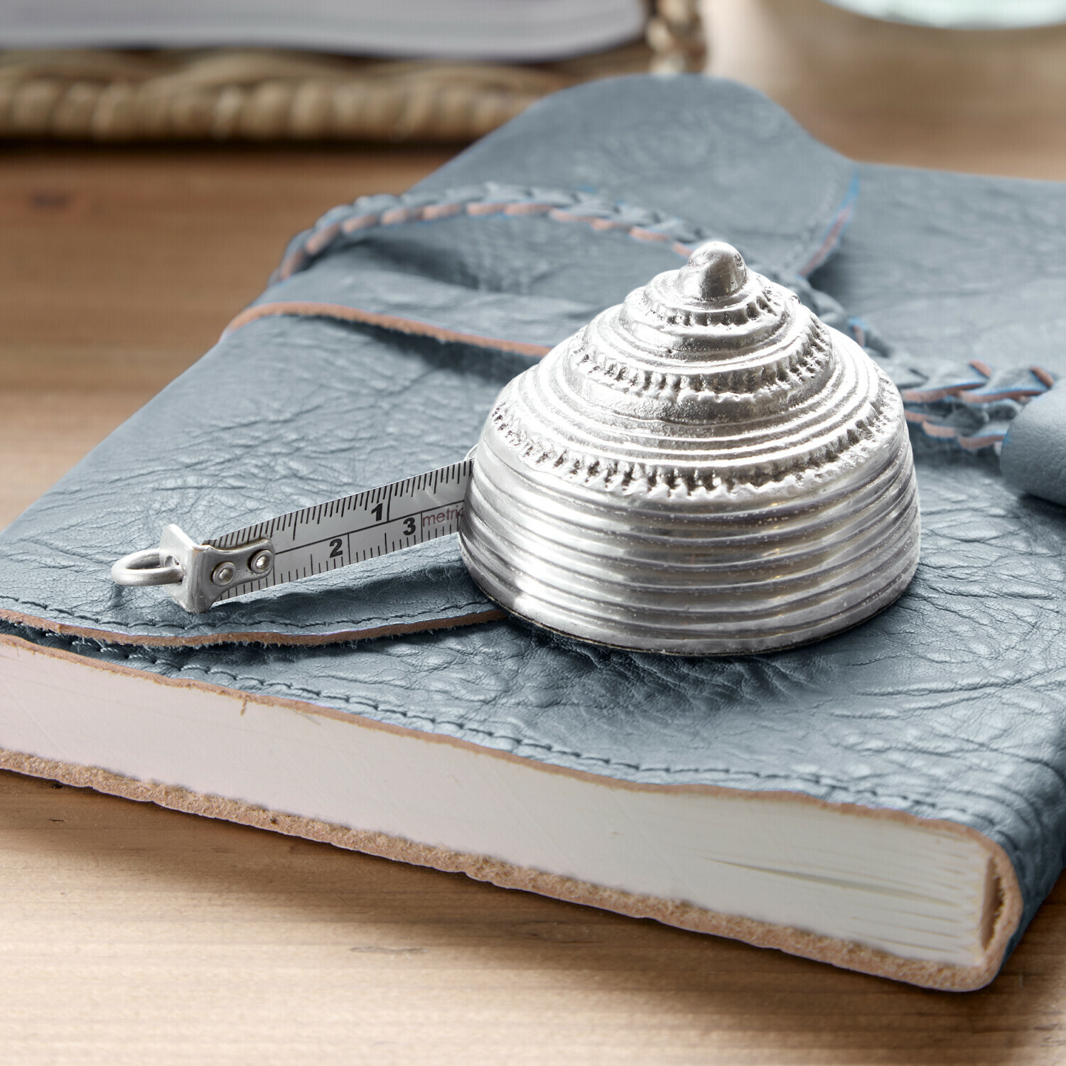 Stříbrné kovové svinovací měřítko ve tvaru mušle na modrém koženém zápisníku
