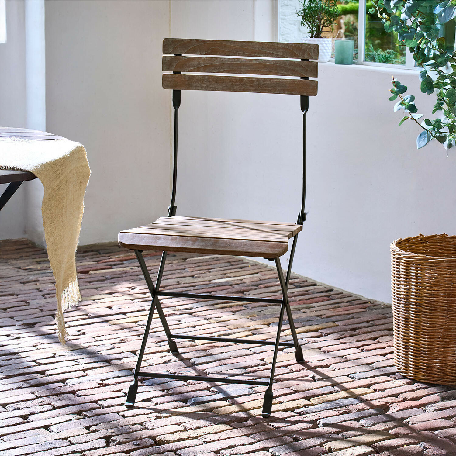 Židle Arémont Skládací dřevěná židle s černým kovovým rámem na cihlové podlaze za denního světla
