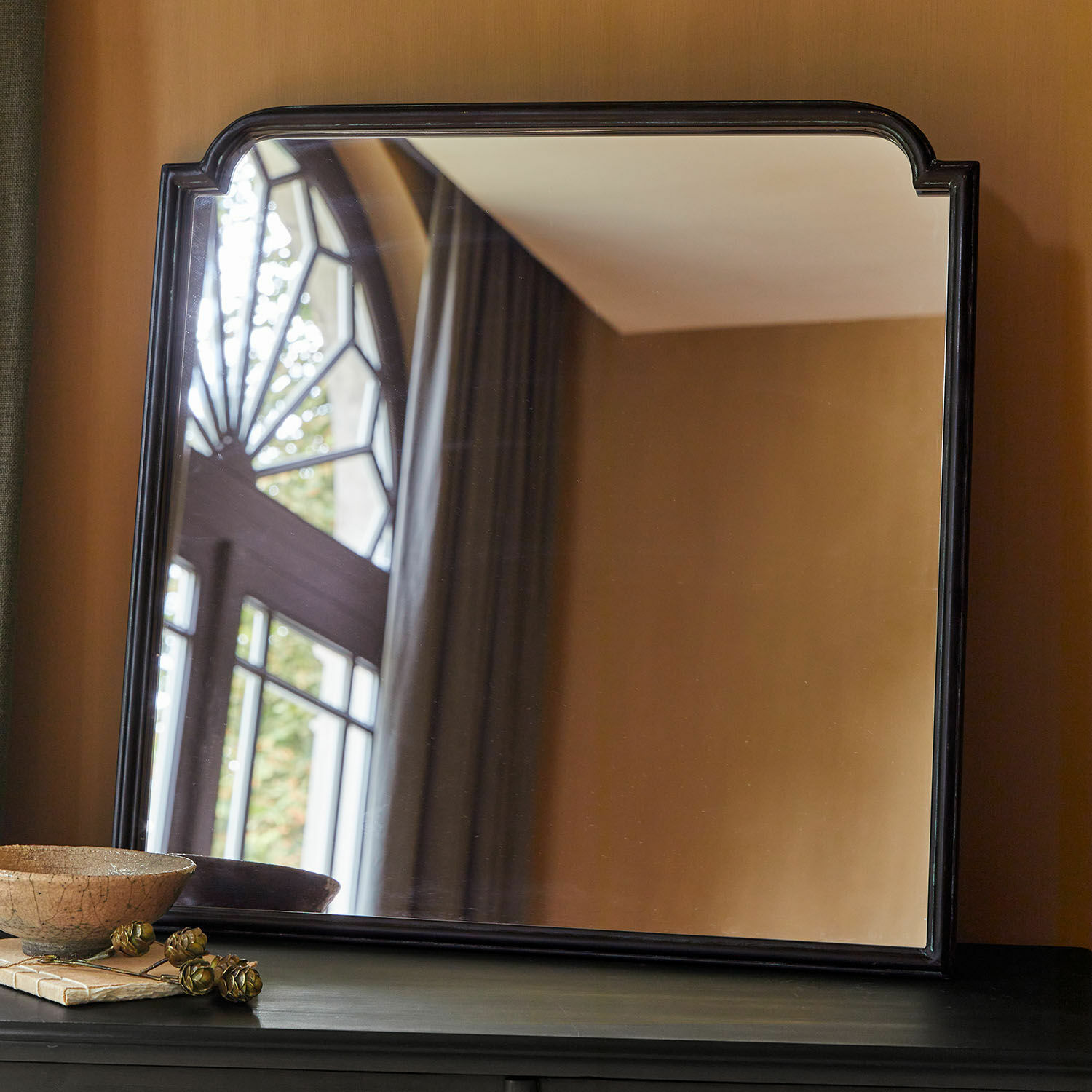 Černý rám zrcadla s oblými rohy na tmavém nábytku v klasickém interiéru
