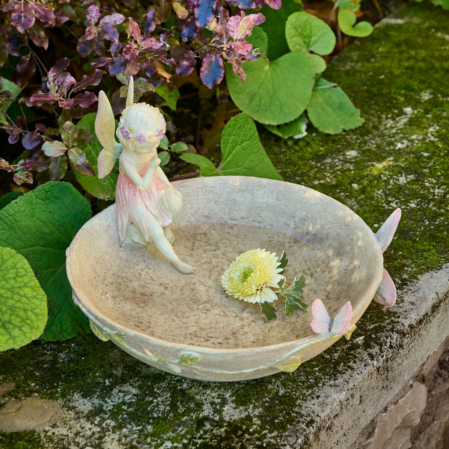 Dekorativní zahradní miska s vílí figurkou a pastelovými motýly na kamenné zdi