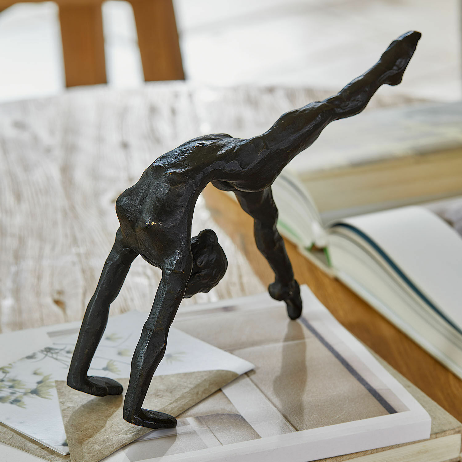 Soška Zayrah Černá kovová soška akrobata v mostu na stole s knihami a papíry