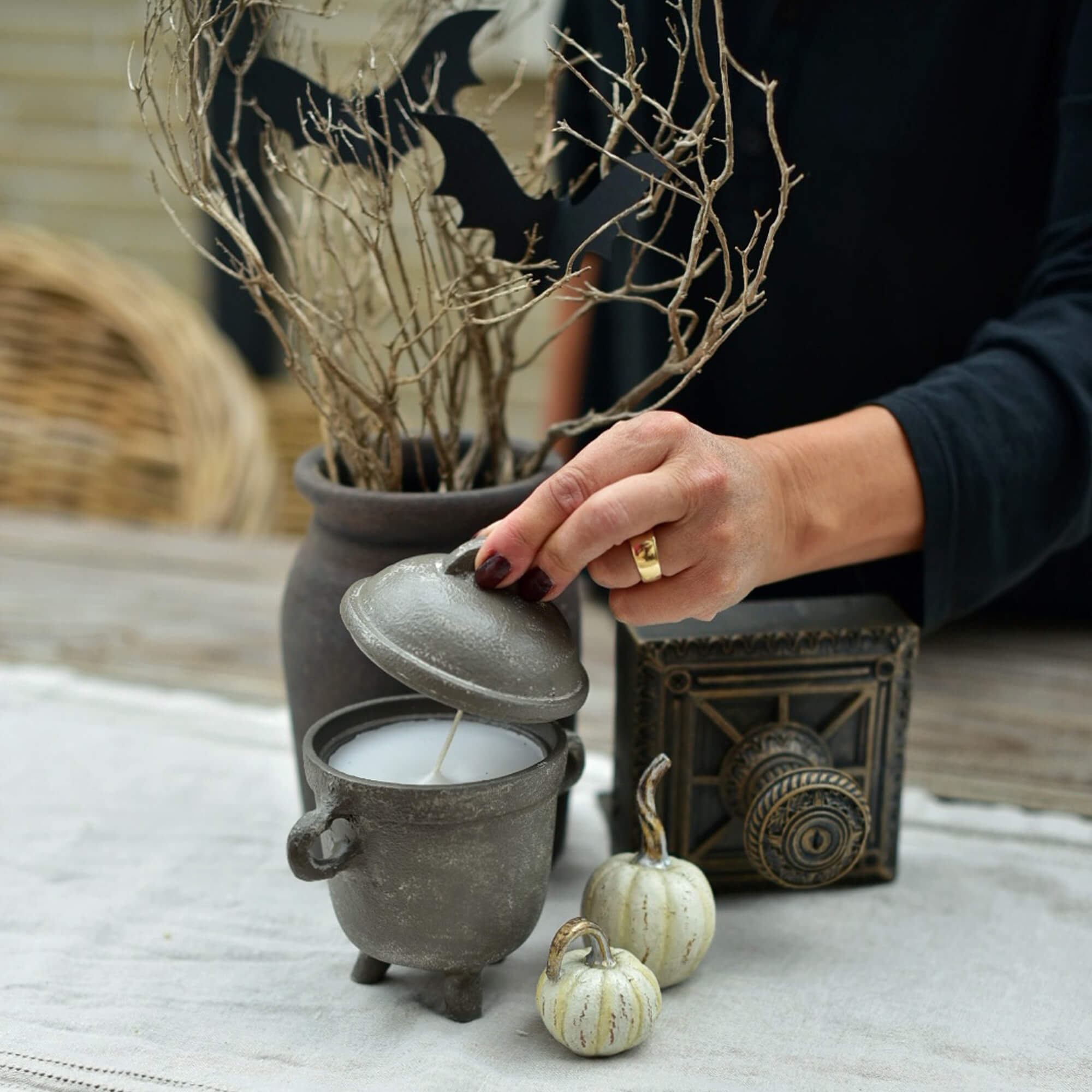 Šedá svíčka ve tvaru kotlíku s víkem na halloweenském stole s dekoracemi z dýní a větví
