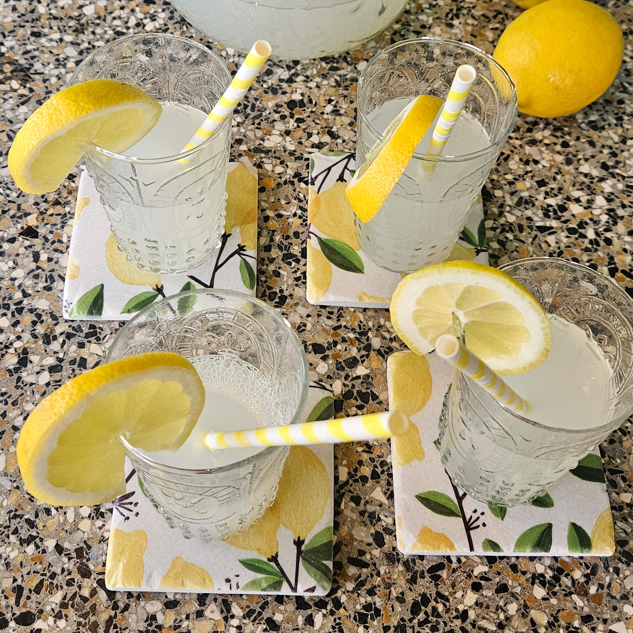 Sklenice s limonádou a plátky citronu na keramických podtáccích s motivem citronů na kamenném povrchu
