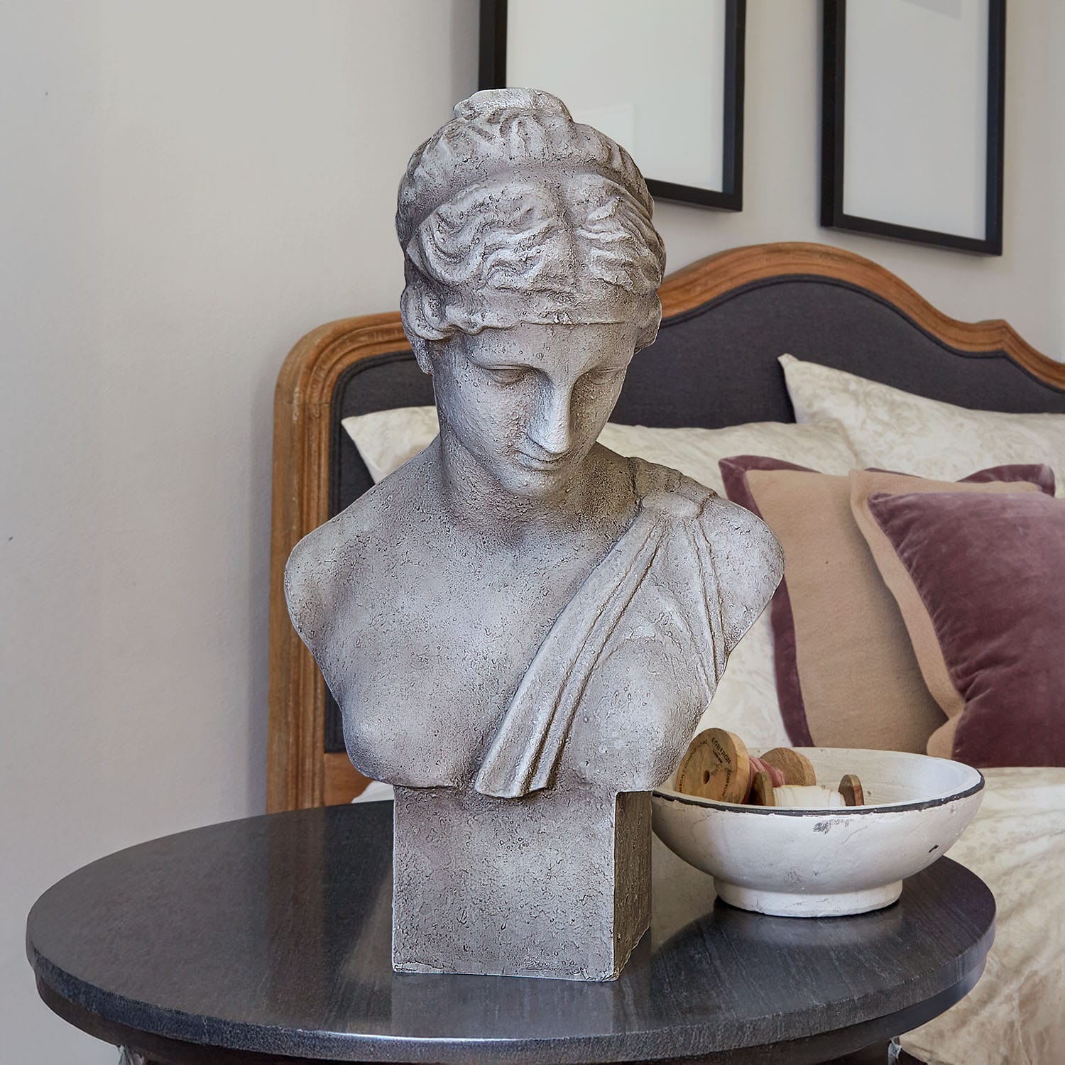 Šedý kamenný bust na černém stole v elegantní ložnici s polštáři
