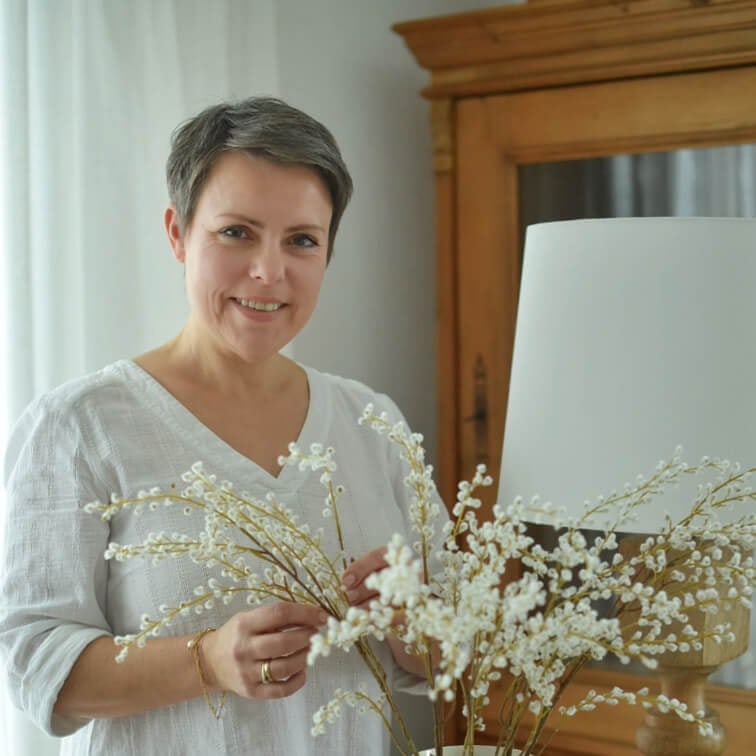Žena v bílém tričku drží dekorativní větve s bílými květy v světlém interiéru