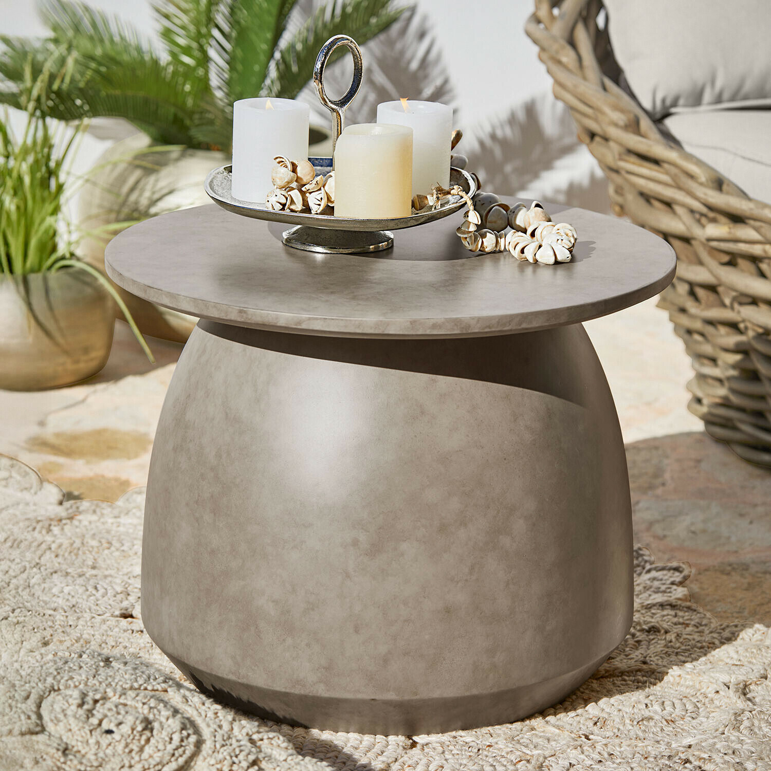 Kulatý šedý betonový stolek s dekorativními svíčkami a mušlemi na terase