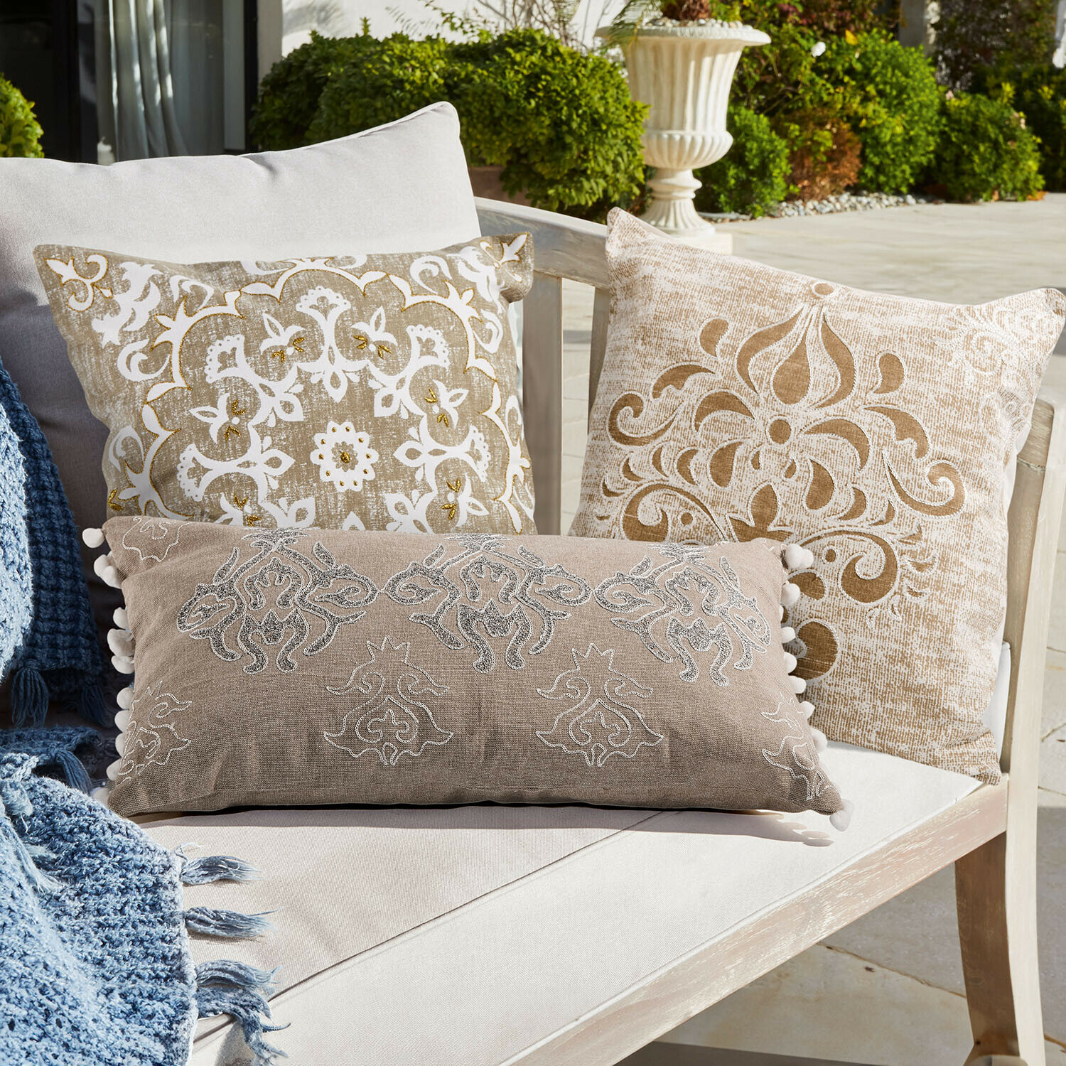 Sada dekorativních polštářů v béžové a bílé barvě s motivy na světlé pohovce venku