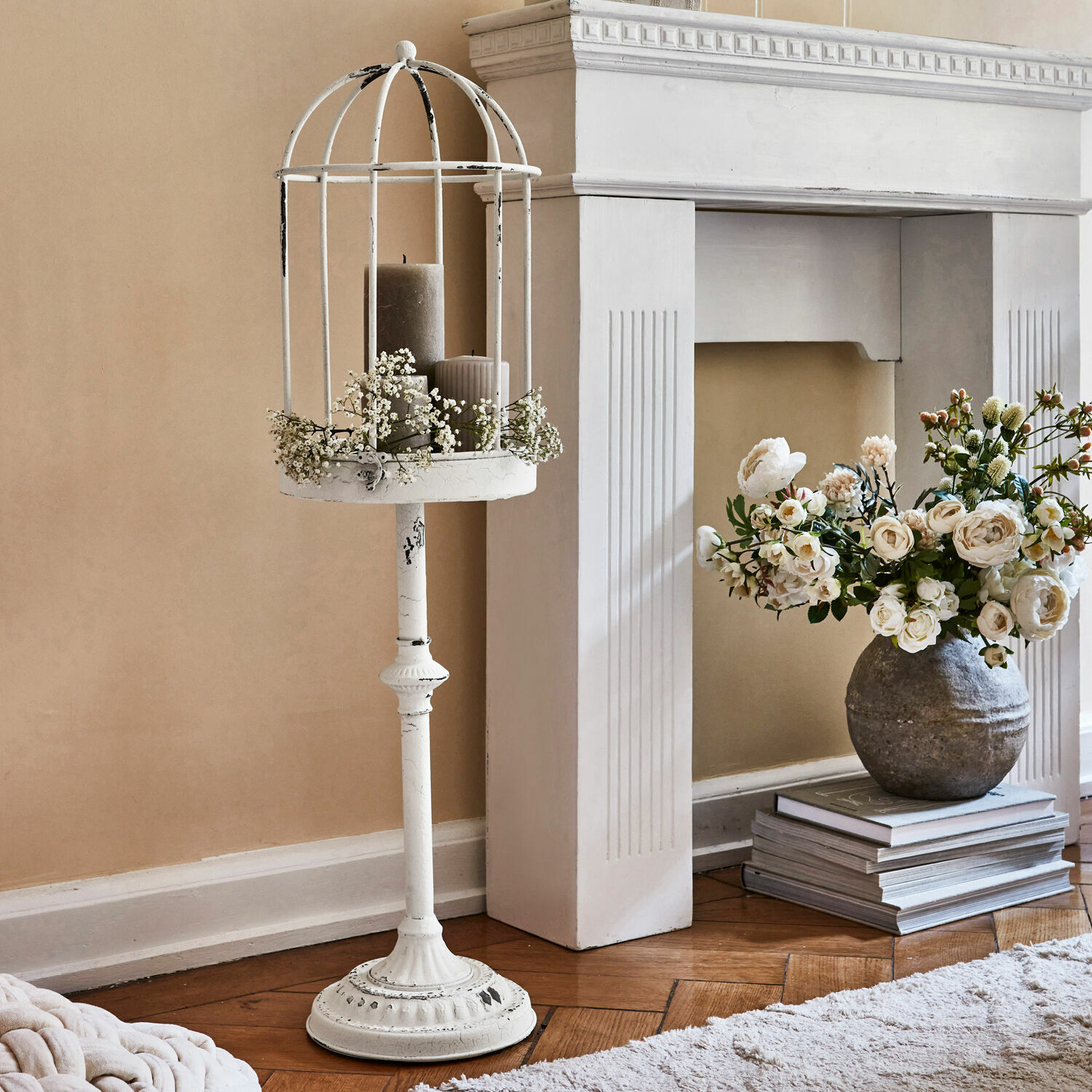 Bílý kovový stojan na svíčky s ozdobnou klecí a šedými svíčkami ve vintage stylu
