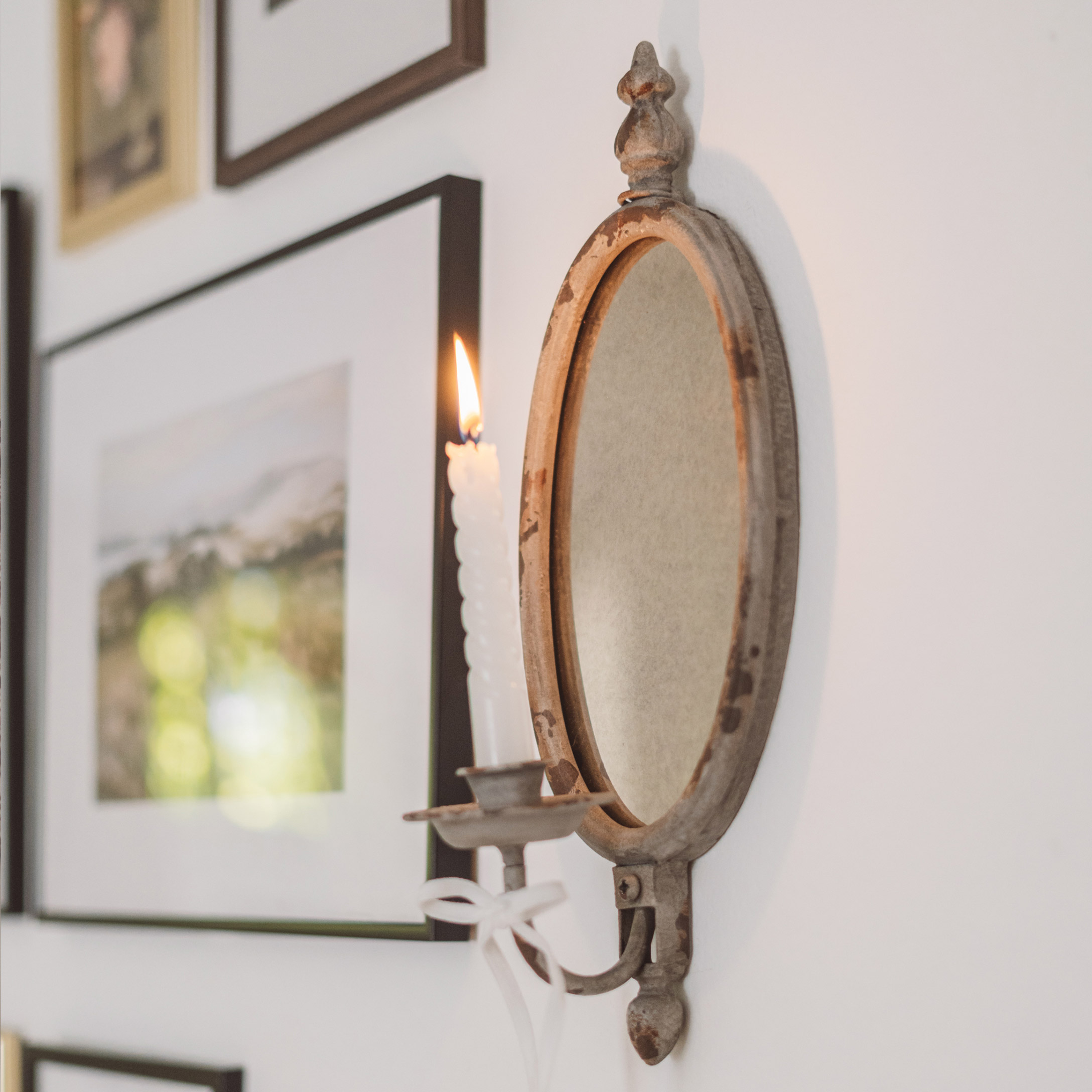 Rustikální kovový nástěnný svícen s oválným zrcadlem a bílou svíčkou ve vintage stylu
