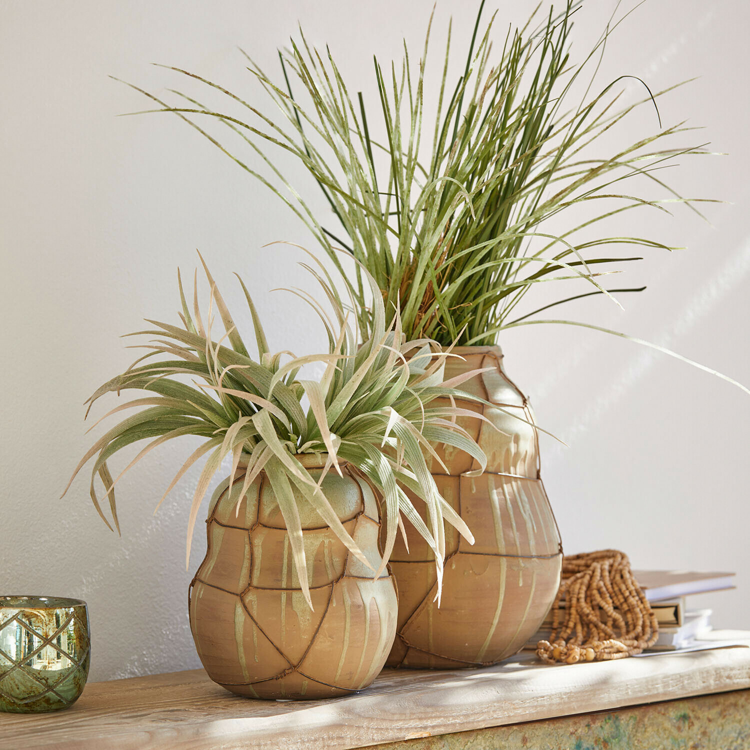 Dvě béžové keramické vázy se zelenými dekorativními rostlinami na dřevěném stole