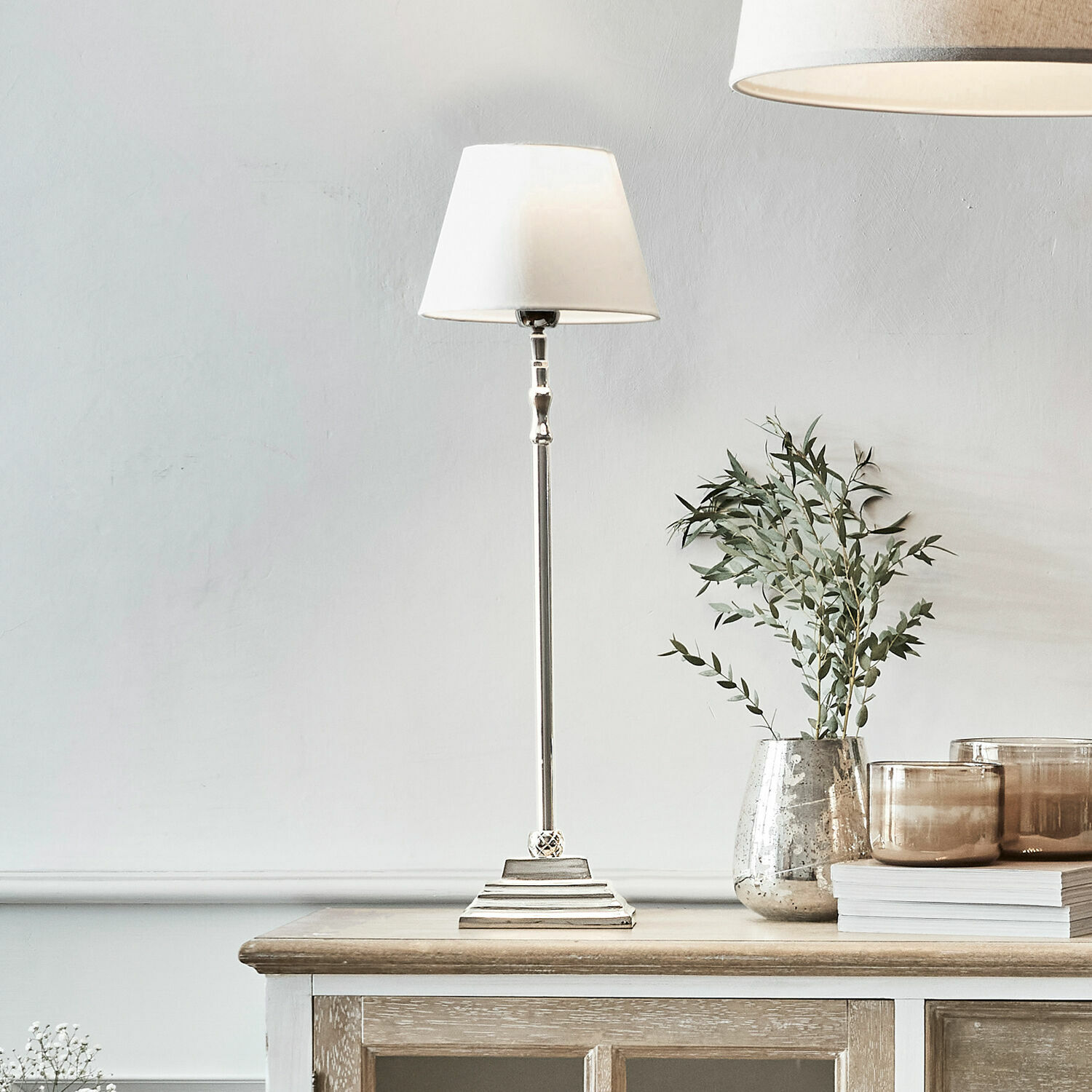 Stolní lampa Mayfair Elegantní stolní lampa s bílým stínidlem a kovovým podstavcem na dřevěném stole, interiérová dekorace
