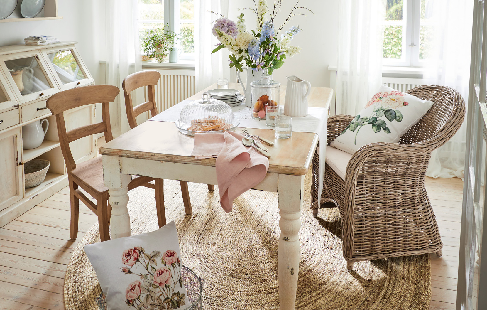 Jídelna ve stylu shabby chic s dřevěným stolem, proutěným křeslem a květinovou výzdobou