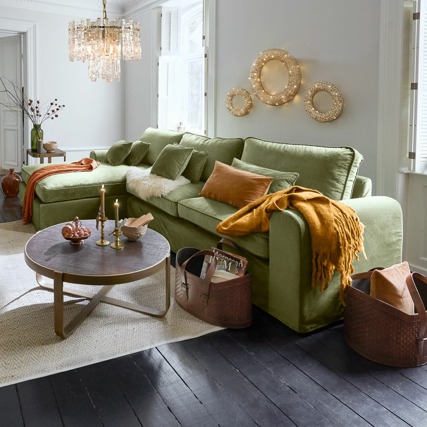 Zelená sametová pohovka s polštáři a oranžovou dekou v moderním obývacím pokoji s dekorativním osvětlením