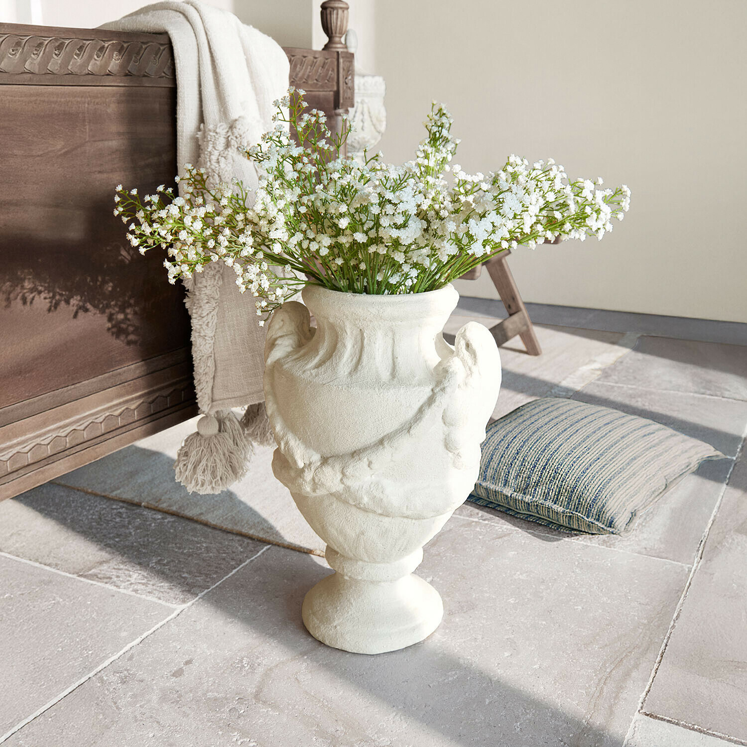 Bílá keramická váza s dekorativním vzorem a bílými květy na kamenné podlaze