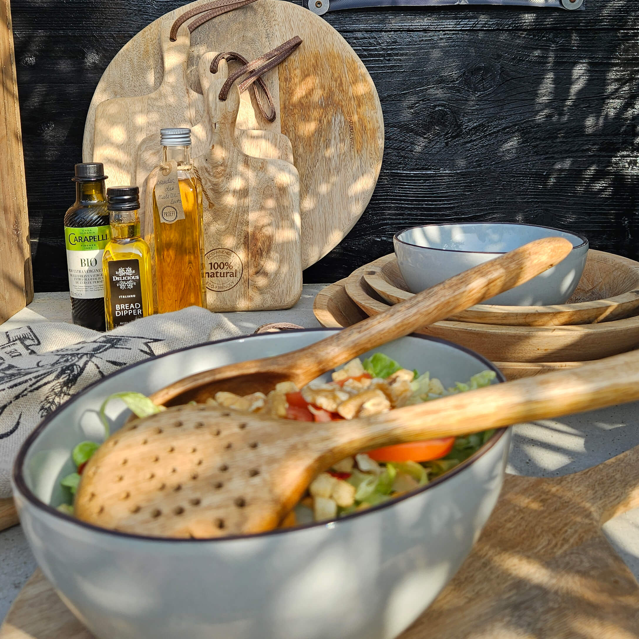 Šedá keramická mísa s dřevěnými příbory a prkénky z přírodního dřeva