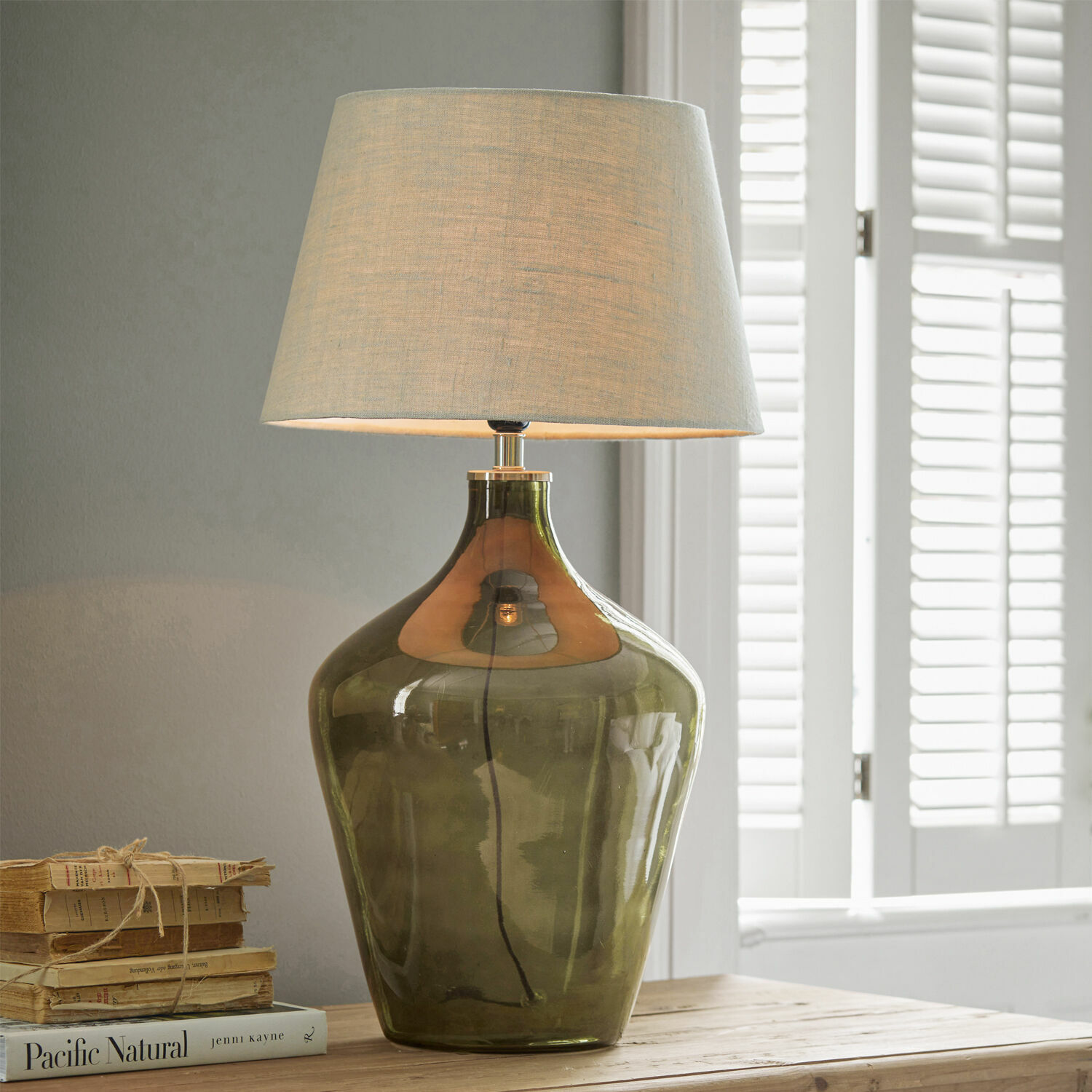 Stolní lampa Morazan Stolní lampa ze zeleného skla s béžovým stínidlem na dřevěném stole vedle knih
