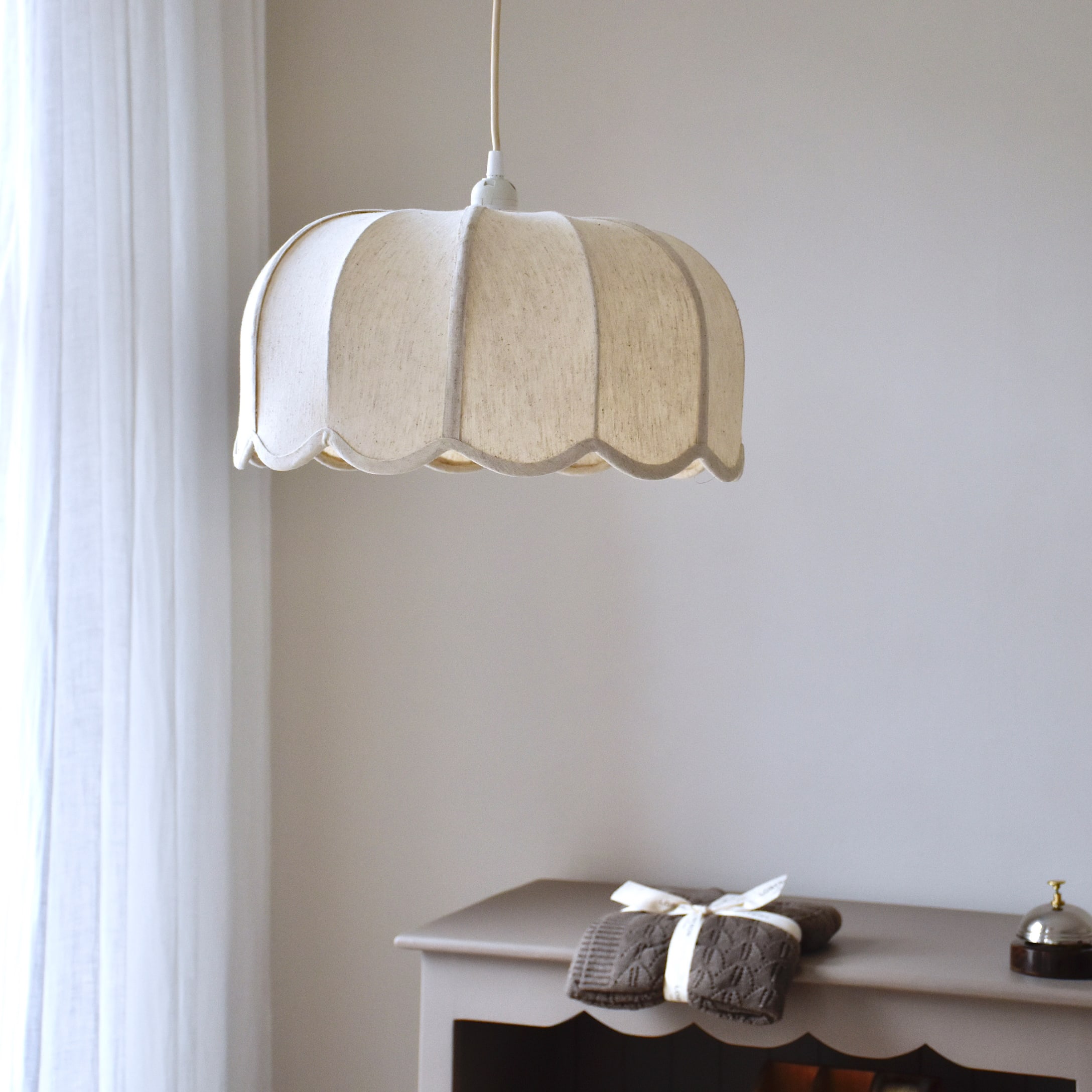 Závěsná lampa z krémové látky s vlnitým tvarem, jemné osvětlení interiéru