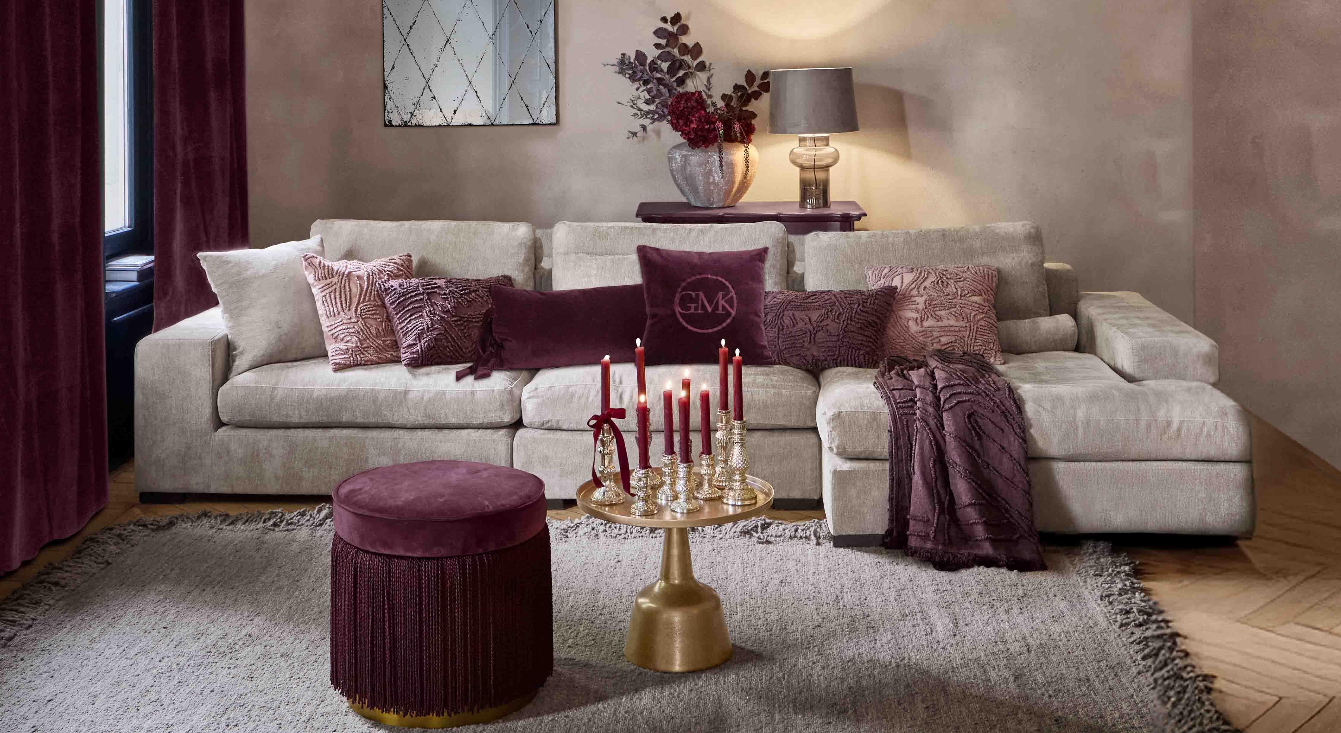 Béžová pohovka s měkkými polštáři a bordovými doplňky v elegantním obývacím pokoji s lampou a zrcadlem