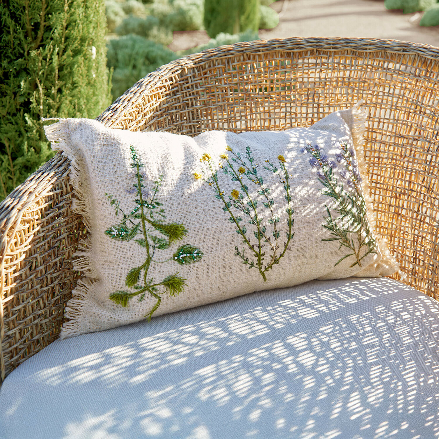 Béžový lněný polštář s rostlinnou výšivkou na proutěném křesle, zahradní dekorace