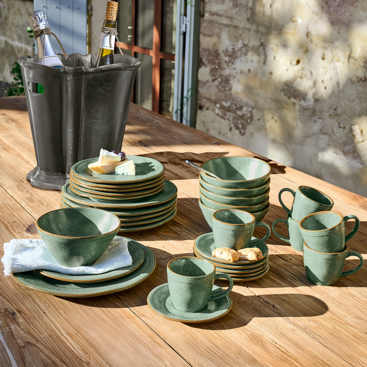 Sada zeleného kameninového nádobí na dřevěném stole s černým vědrem na víno